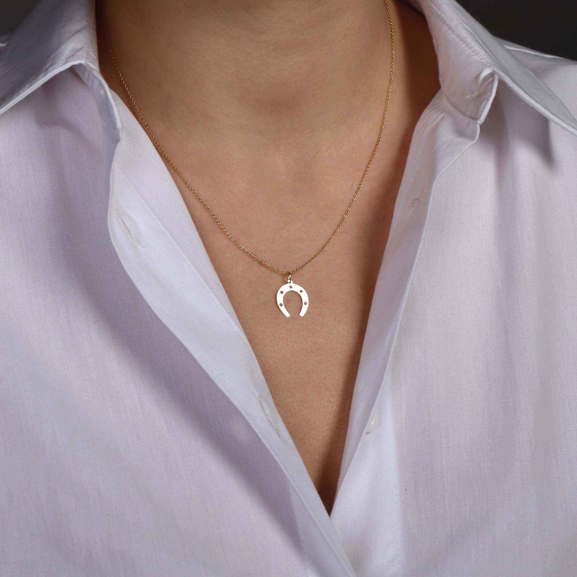 Gold necklace with a horseshoe pendant worn by a person in a white shirt.