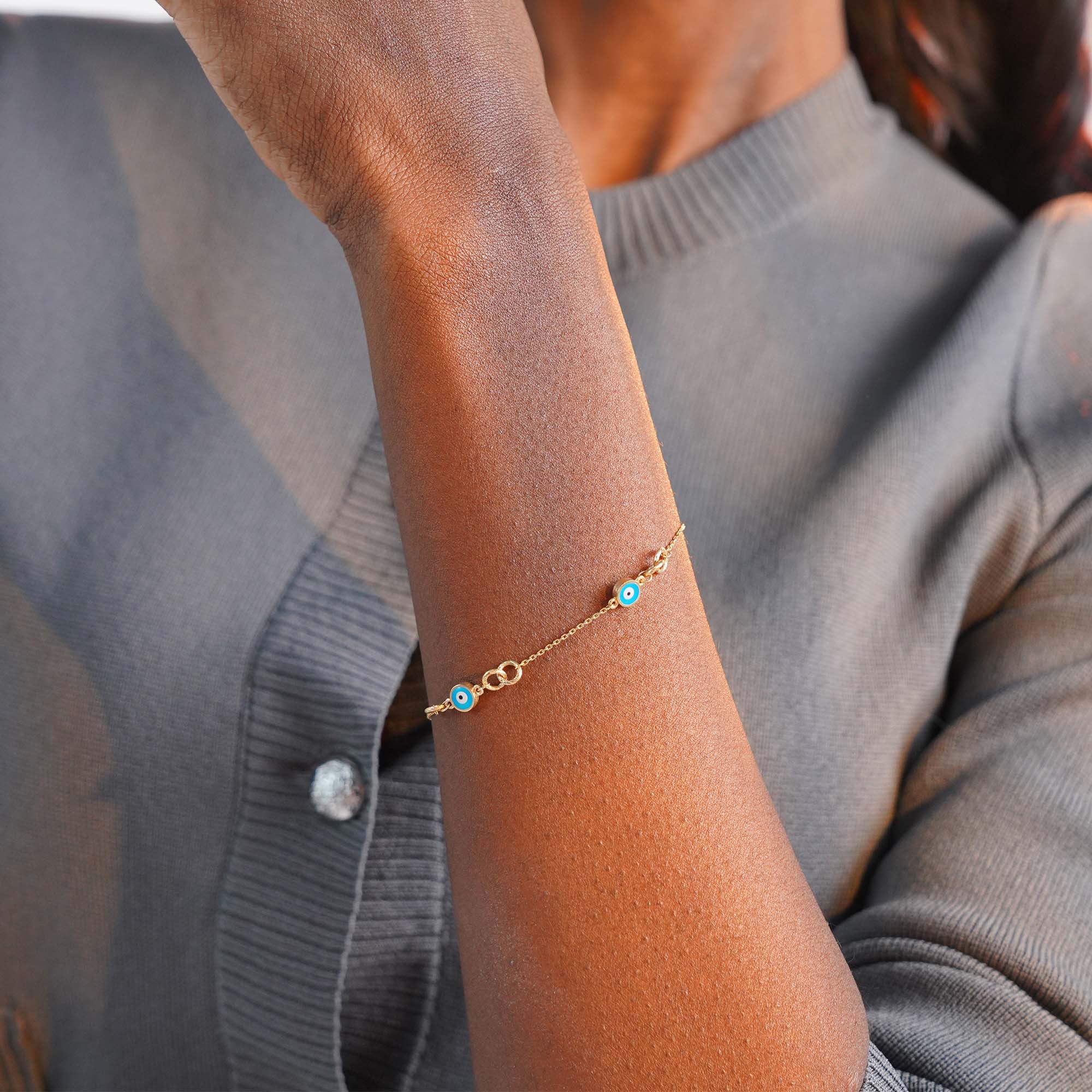 Gold bracelet with a blue evil eyes on a person's wrist against a light gray background