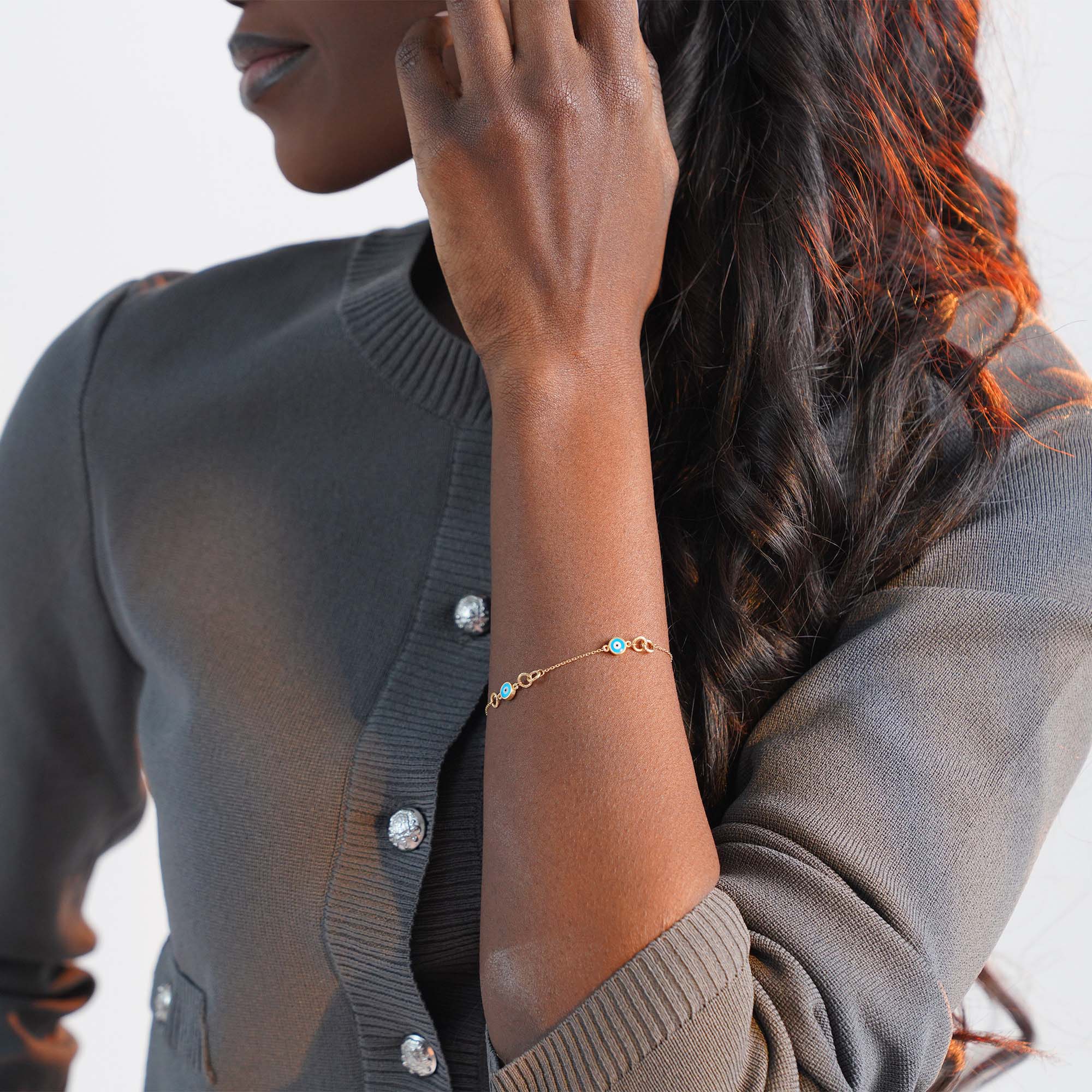 Person wearing a gold bracelet with turquoise evil eyes on a blurred background
