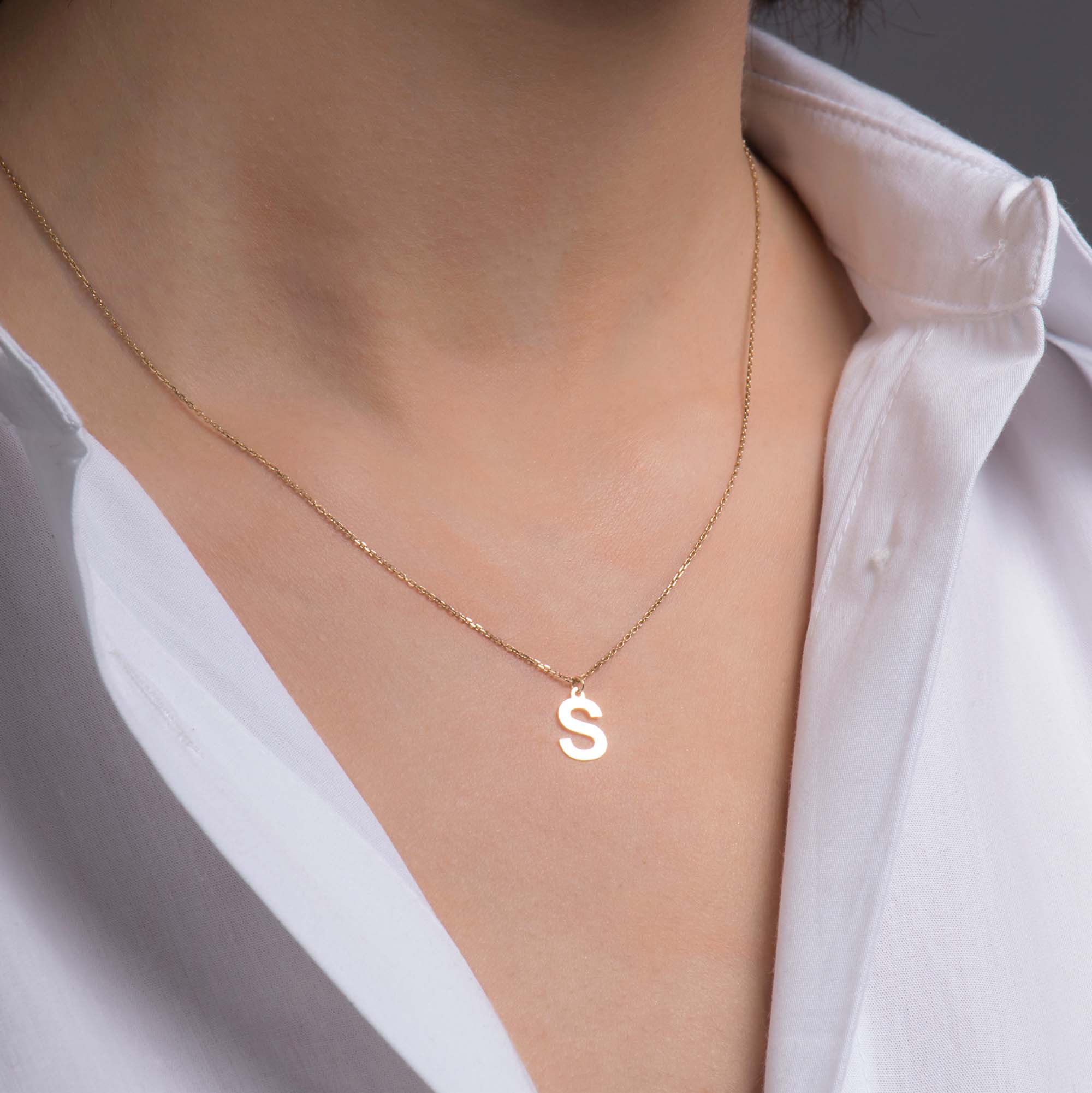 Gold necklace with a 'S' pendant worn by a person in a white shirt.