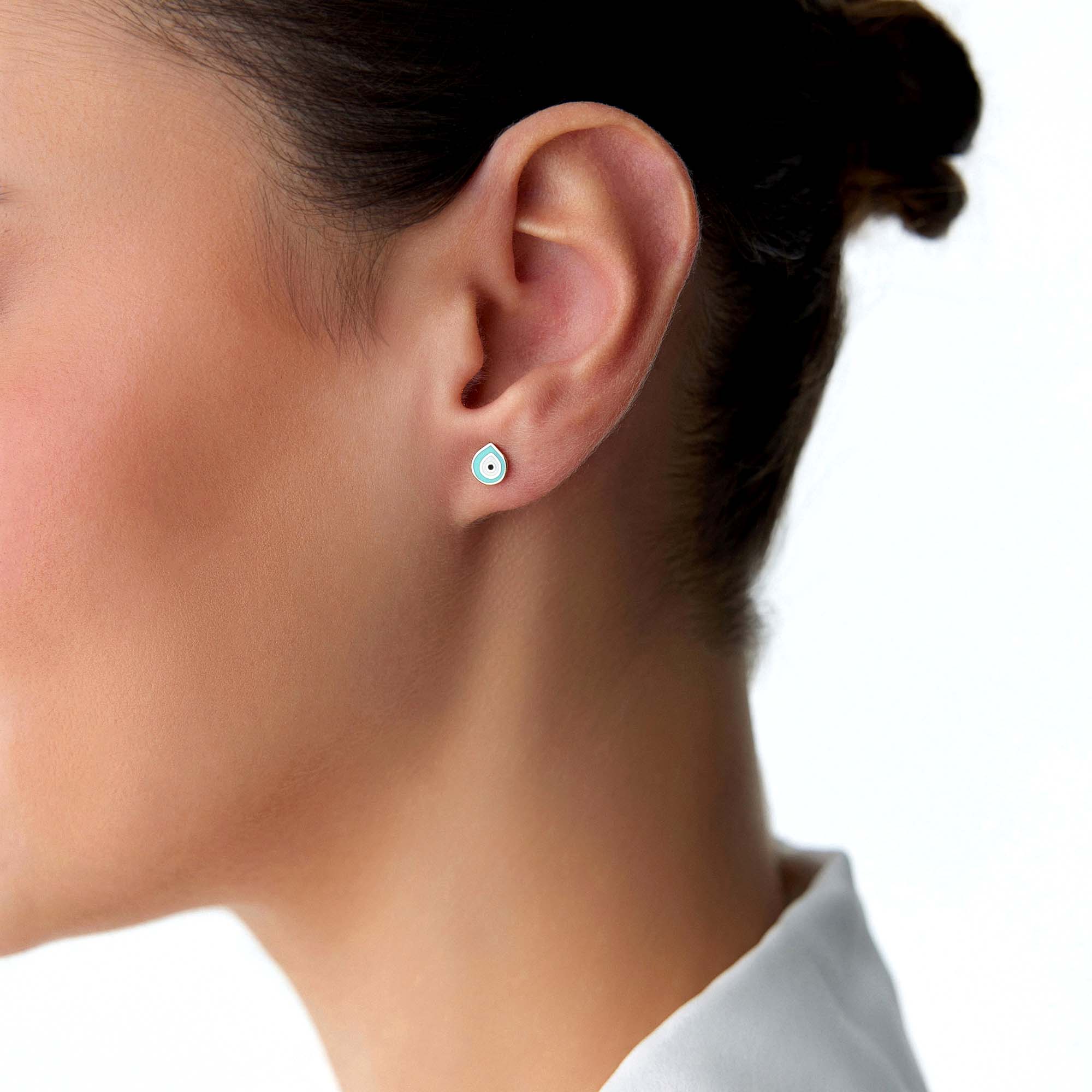 Close-up of an ear wearing a small raindrop shaped evil eye stud.