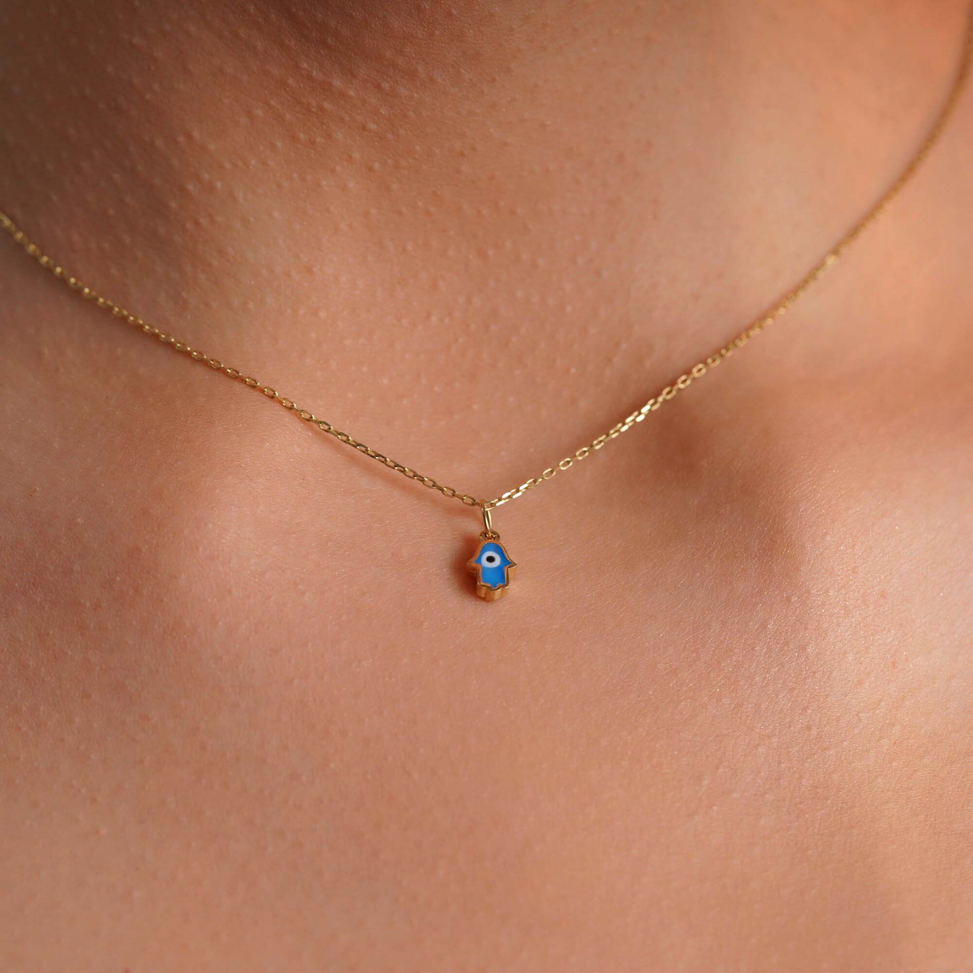 A model wearing a tiny hamsa pendant with an evil eye center worn on a thin gold chain.