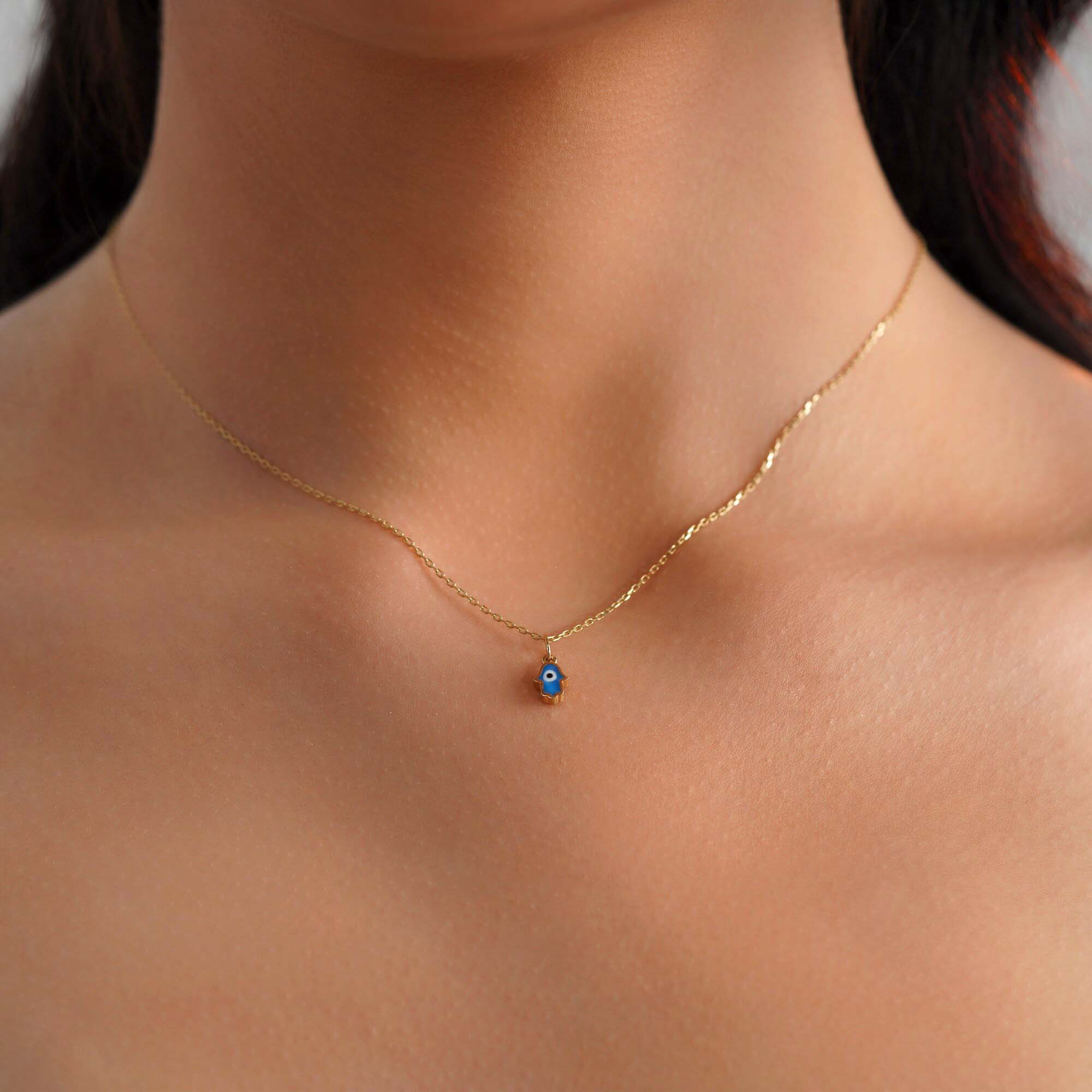 A model wearing a tiny hamsa pendant with an evil eye center worn on a thin gold chain.