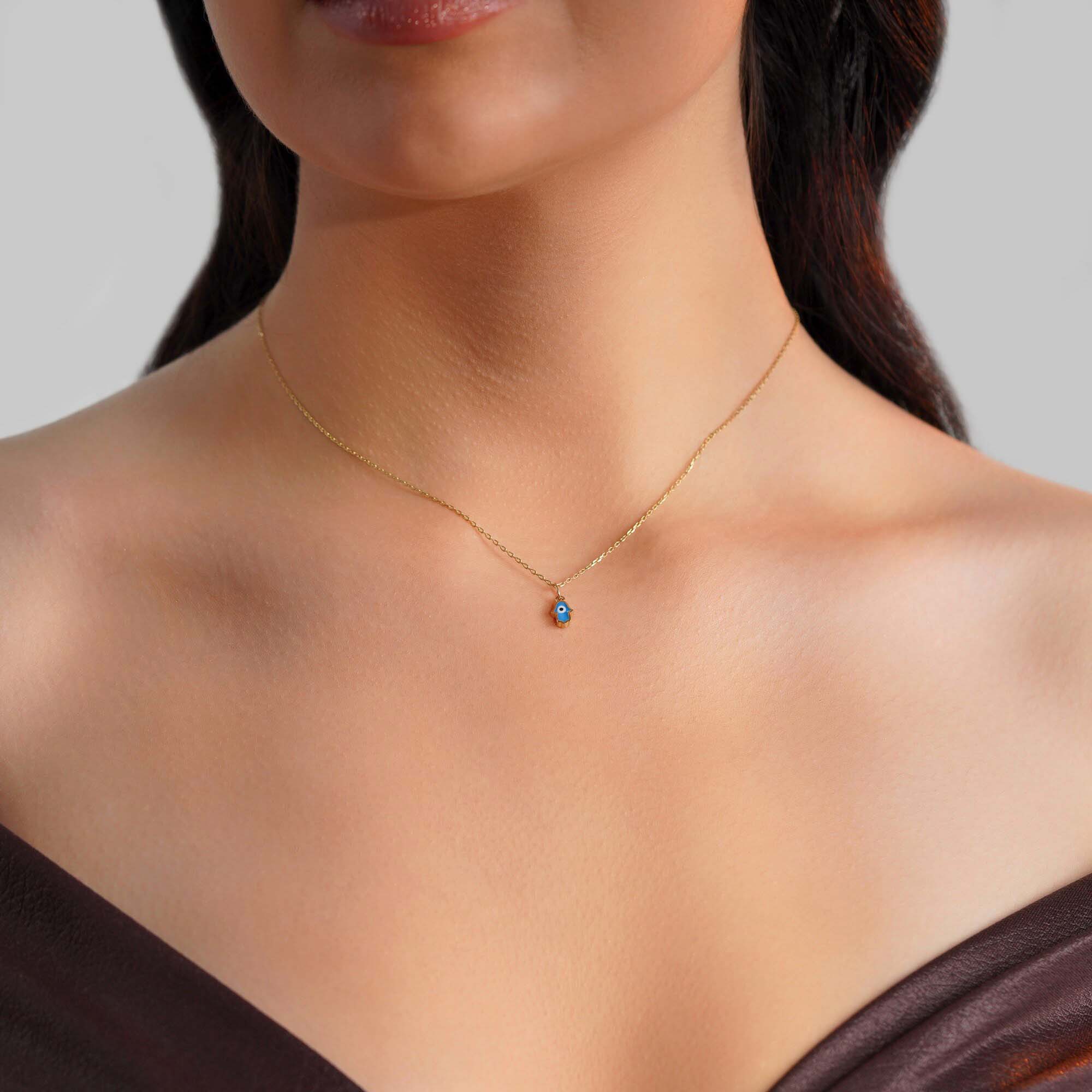 A model wearing a tiny hamsa pendant with an evil eye center worn on a thin gold chain.