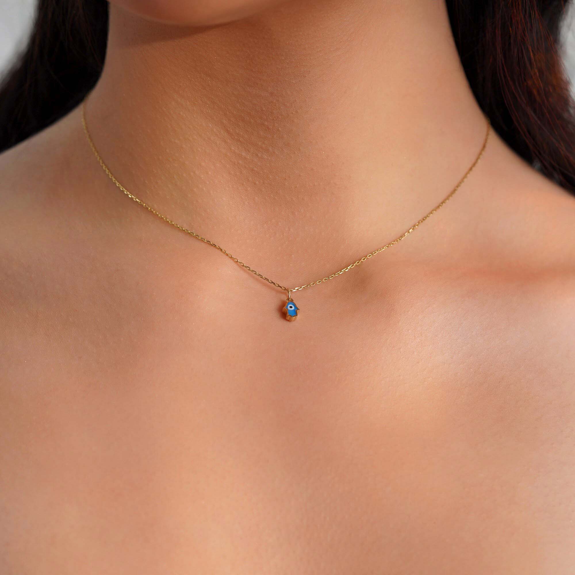 A model wearing a tiny hamsa pendant with an evil eye center worn on a thin gold chain.