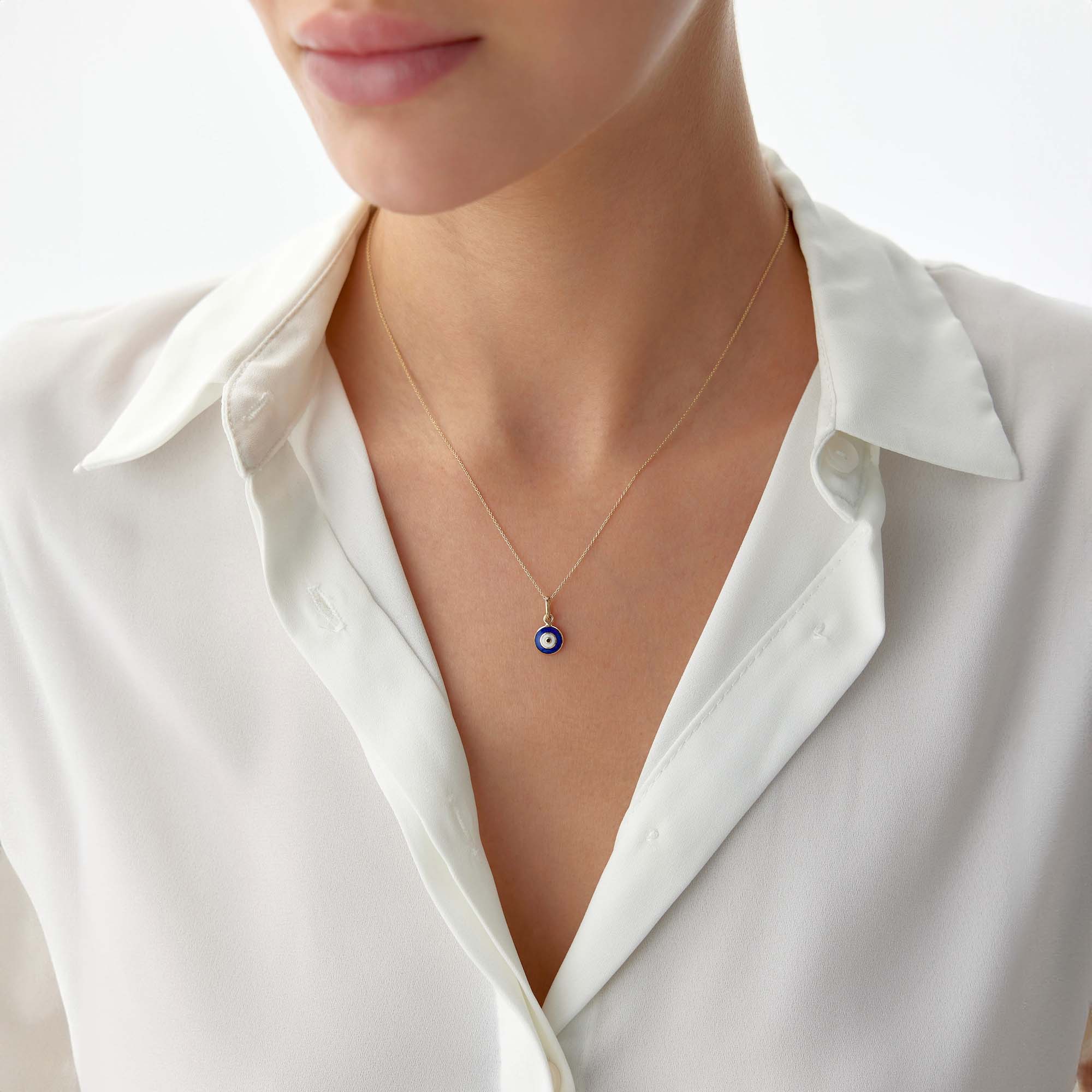 A model wearing a 14k yellow gold tiny navy blue evil eye pendant on a thin gold chain.