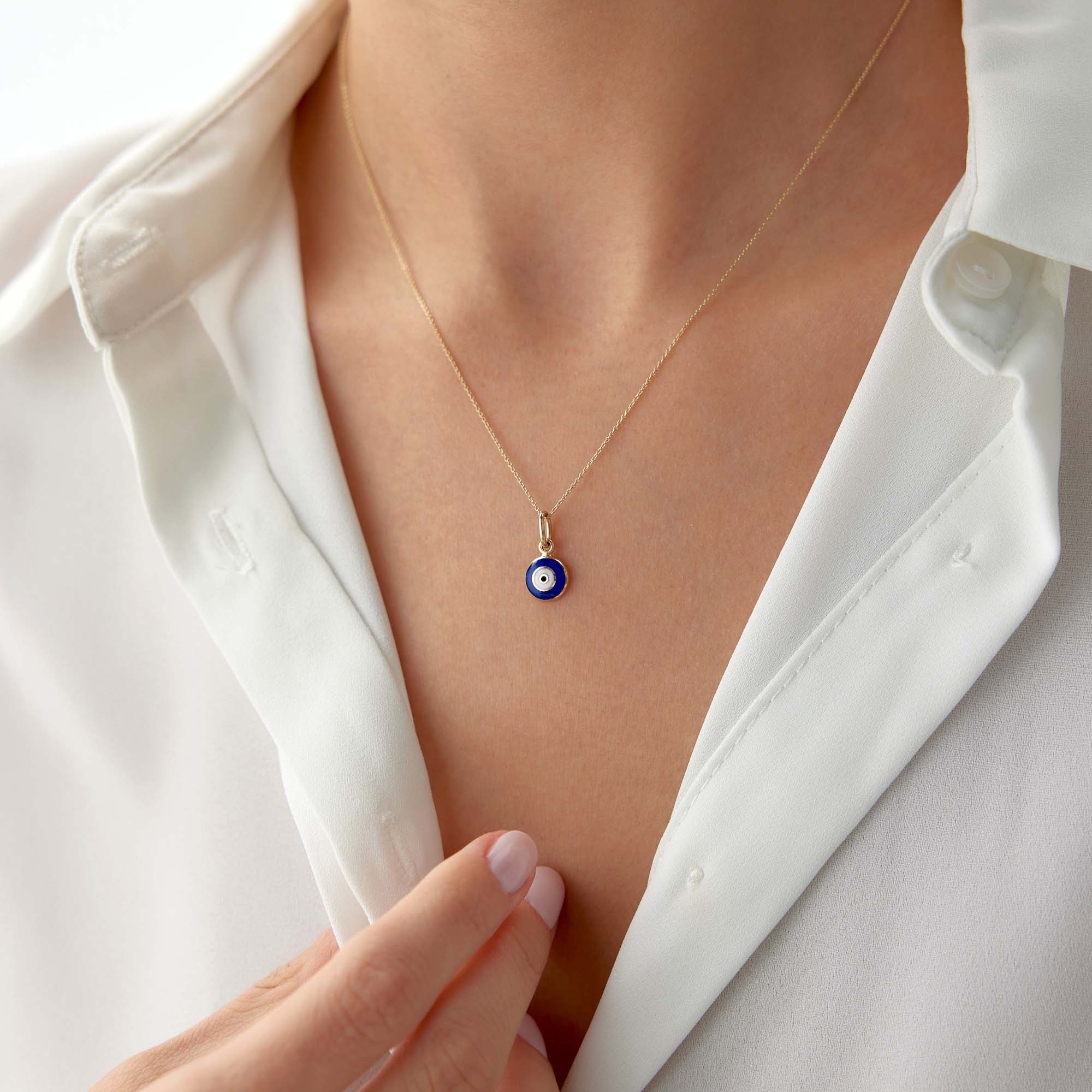 A model wearing a 14k yellow gold tiny navy blue evil eye pendant on a thin gold chain.