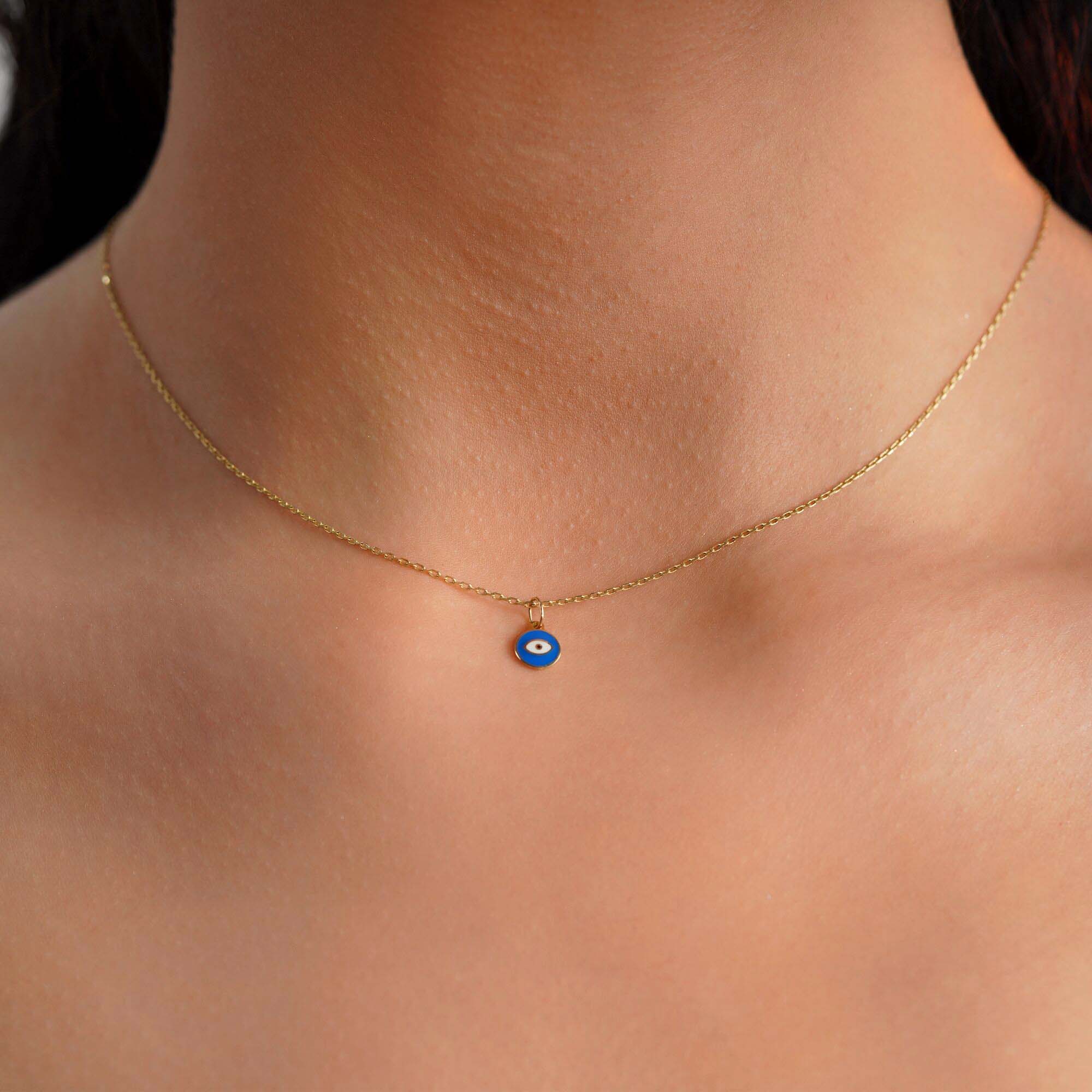 A tiny eye pendant worn by a model on a thin gold chain.