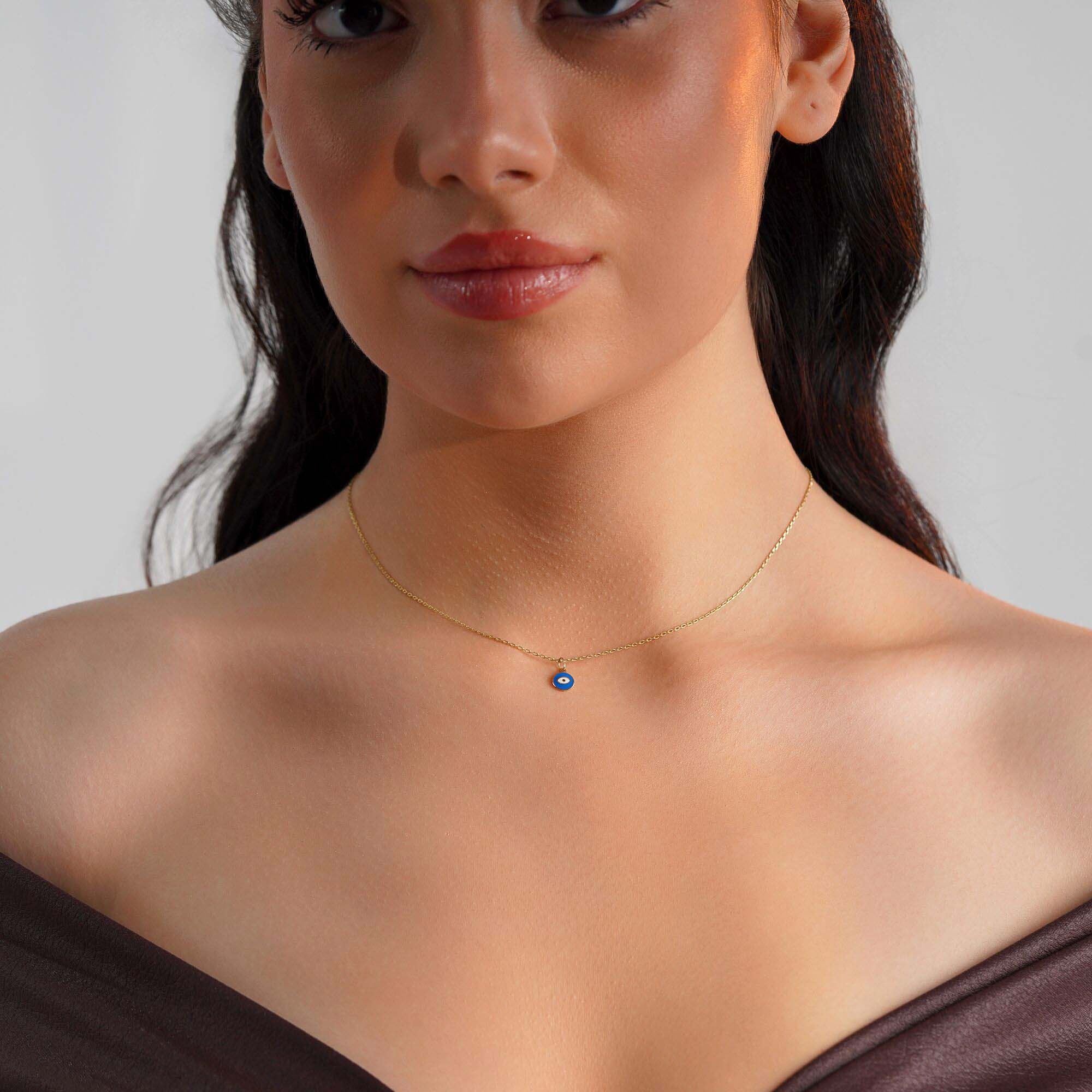 A tiny eye pendant worn by a model on a thin gold chain.