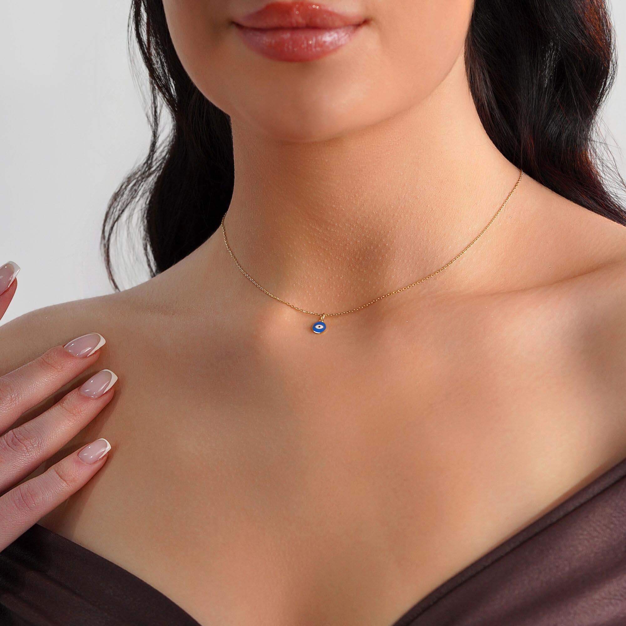 A tiny eye pendant worn by a model on a thin gold chain.