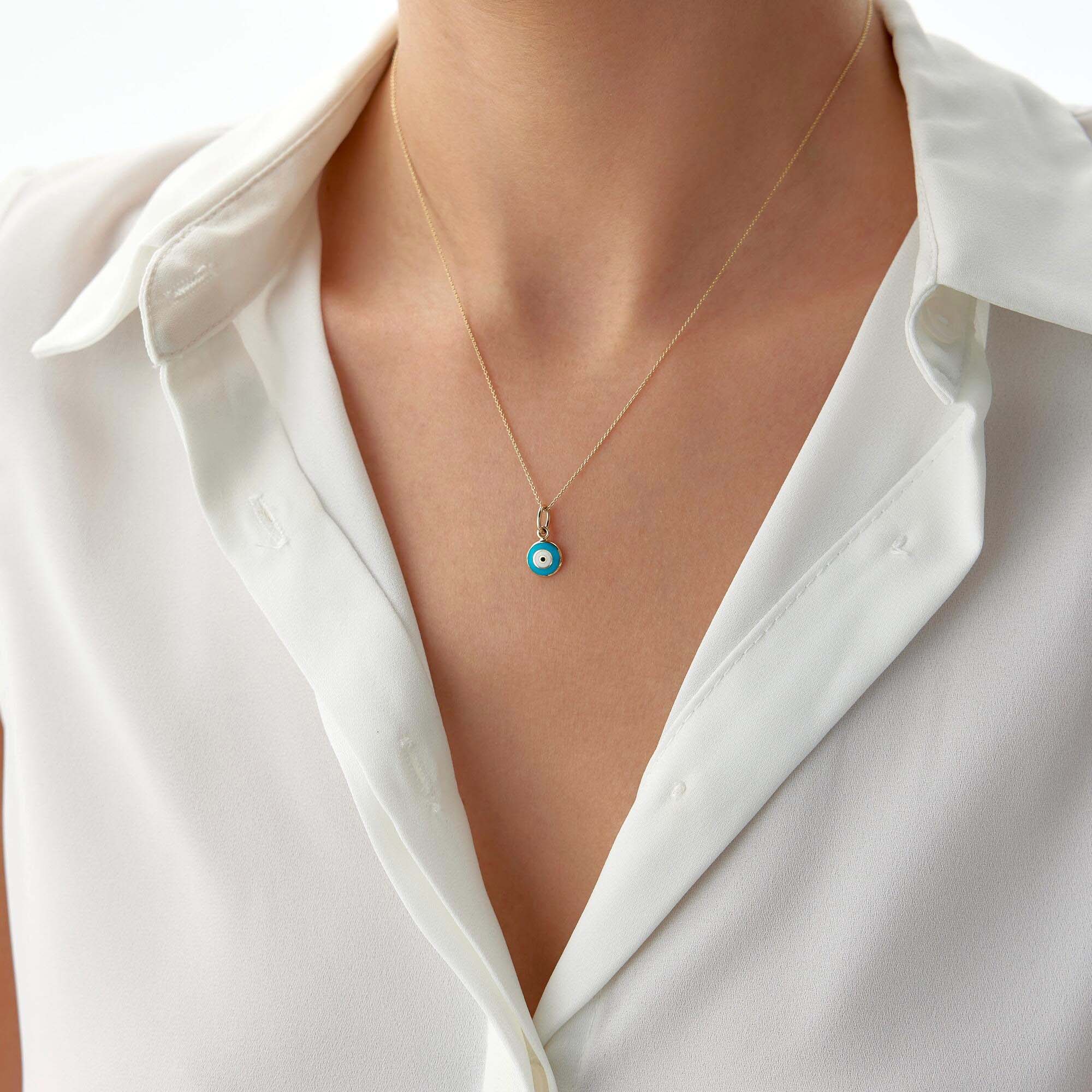 A tiny turquoise color evil eye pendant shown on a thin gold chain worn by a model.
