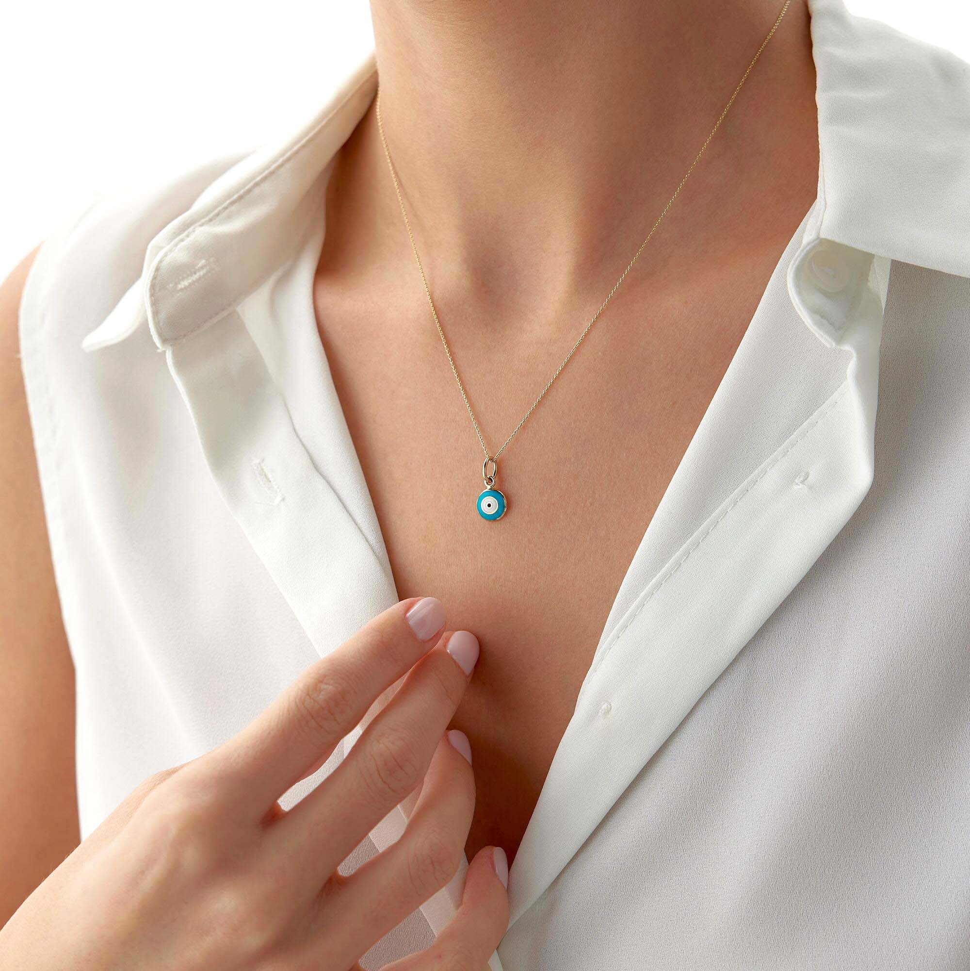 A tiny turquoise color evil eye pendant shown on a thin gold chain worn by a model.
