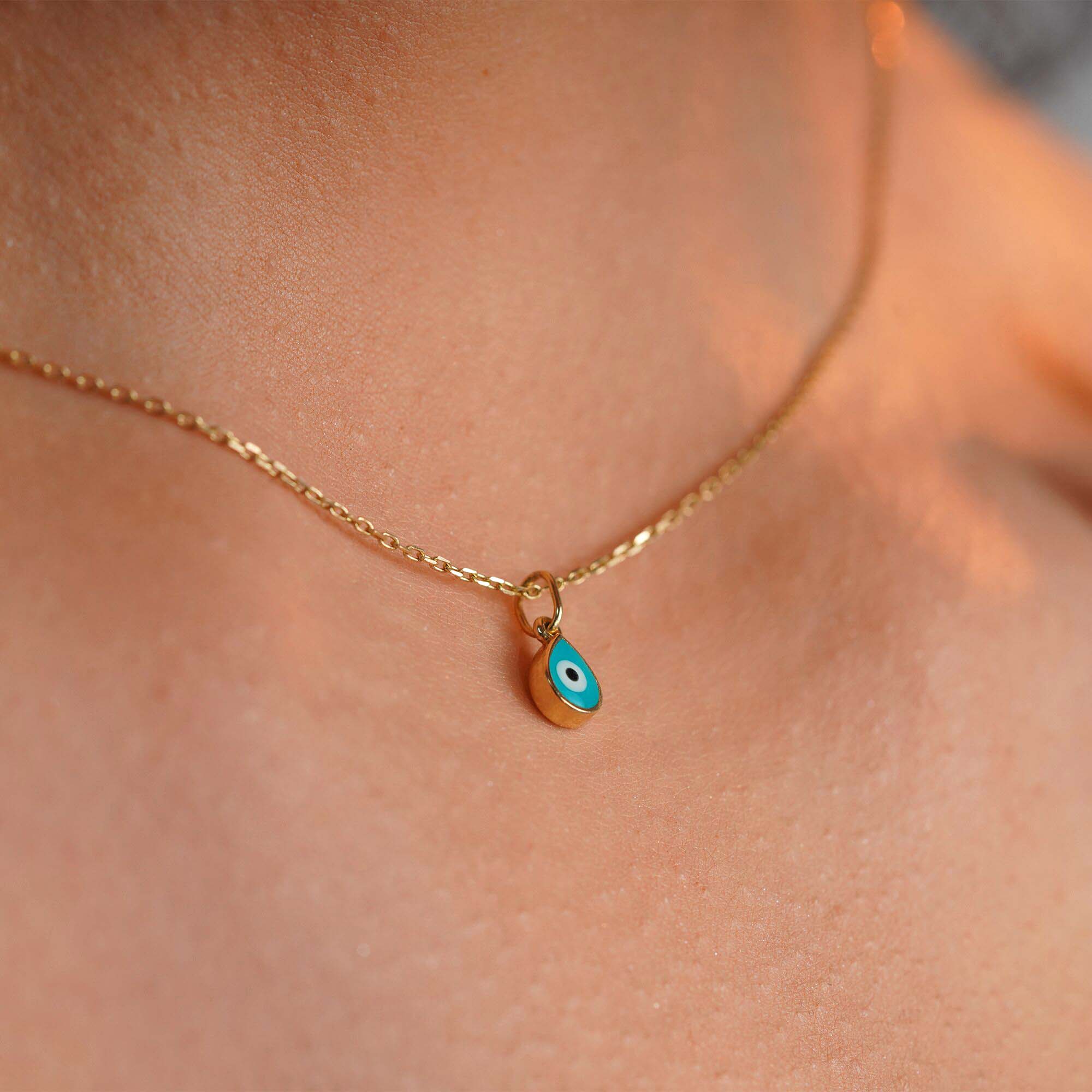 A model wearing a tiny turquoise raindrop pendant on a thin chain shown up-close