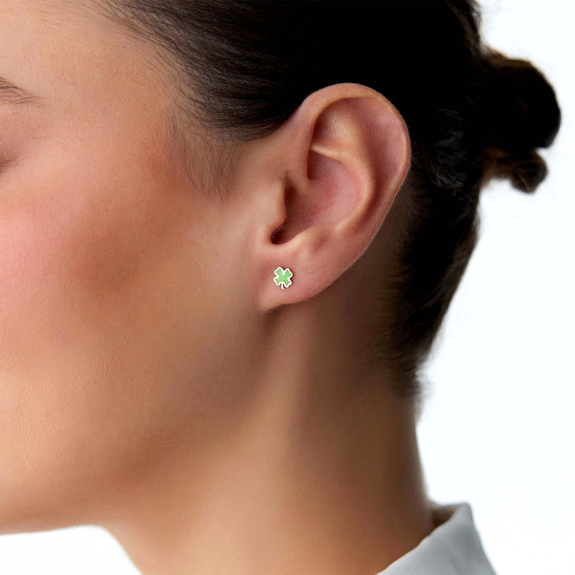 Close-up of an ear wearing a green four-leaf clover earring on a white background