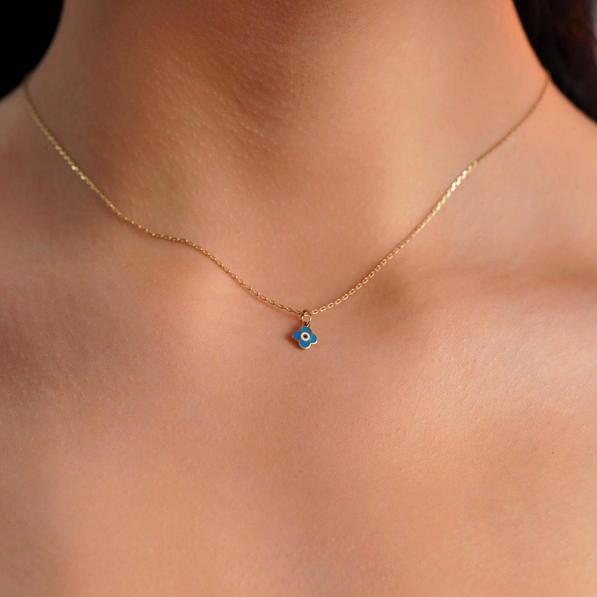 A model wearing a tiny clover pendant with an evil eye center worn on a thin gold chain.