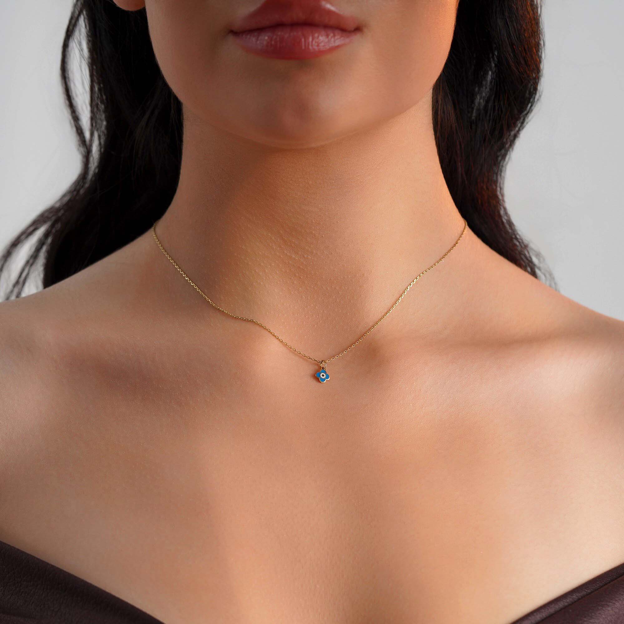 A model wearing a tiny clover pendant with an evil eye center worn on a thin gold chain.