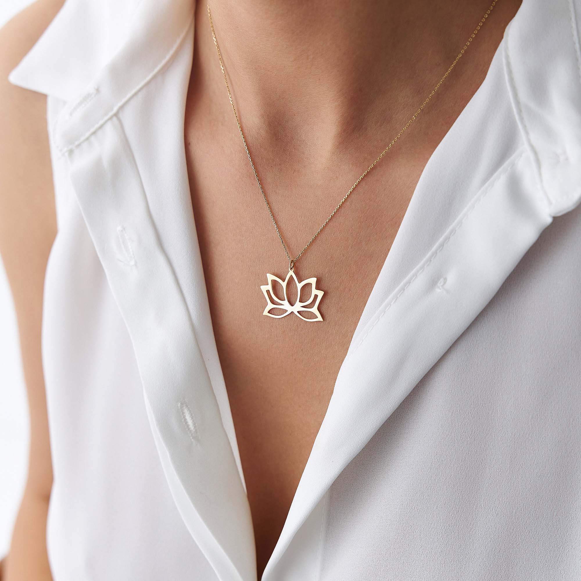 Gold necklace with a lotus flower pendant worn by a person in a white shirt.