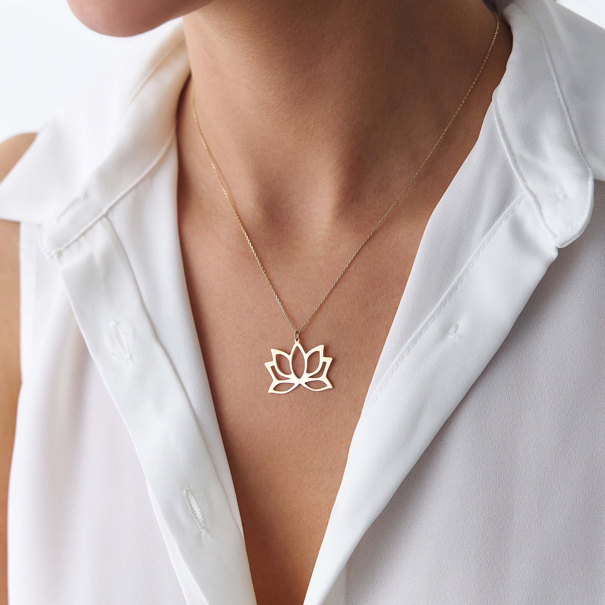 Gold lotus flower necklace worn by a person in a white shirt