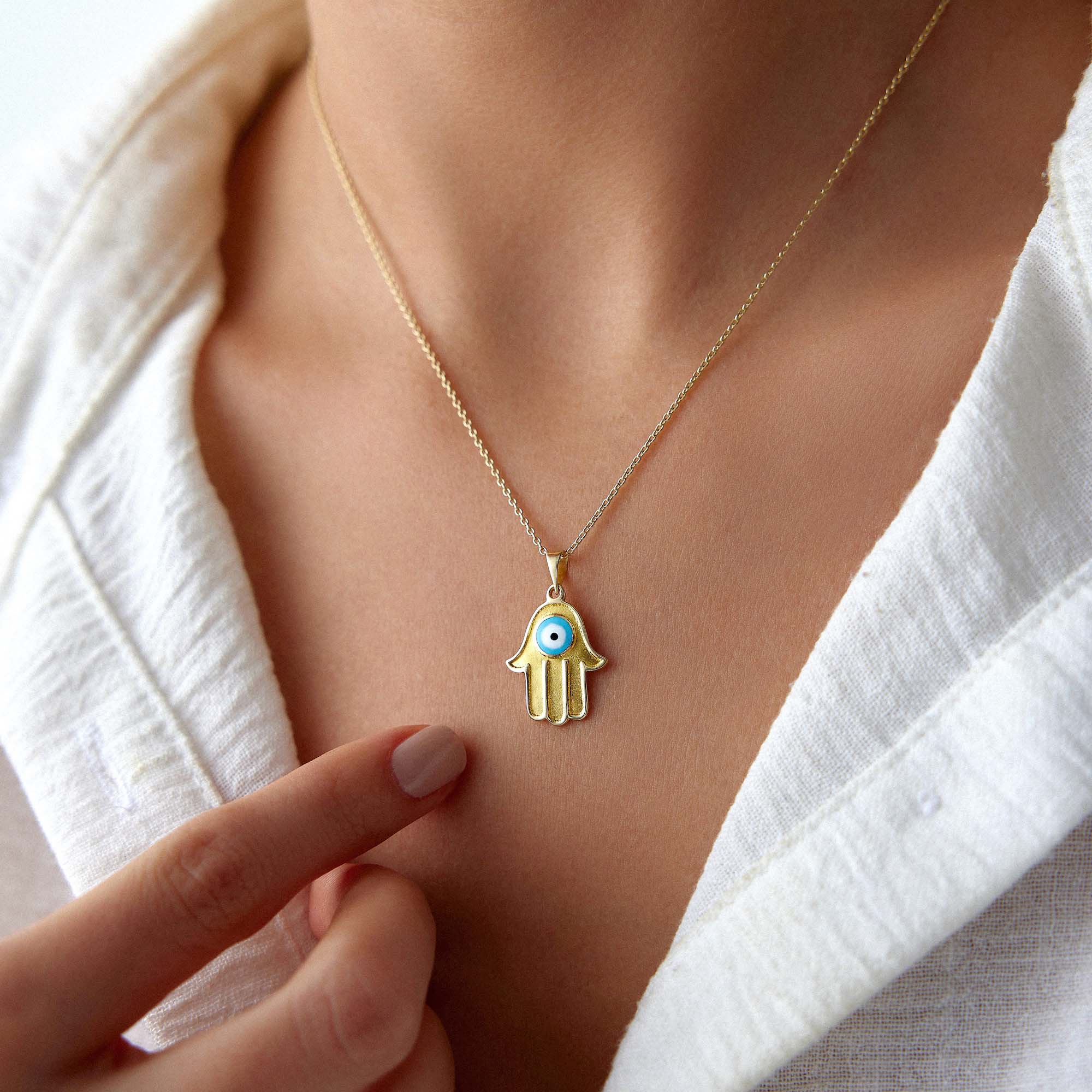 A 14k yellow gold necklace with a hamsa hand pendant featuring a turquoise evil eye, worn by a person.