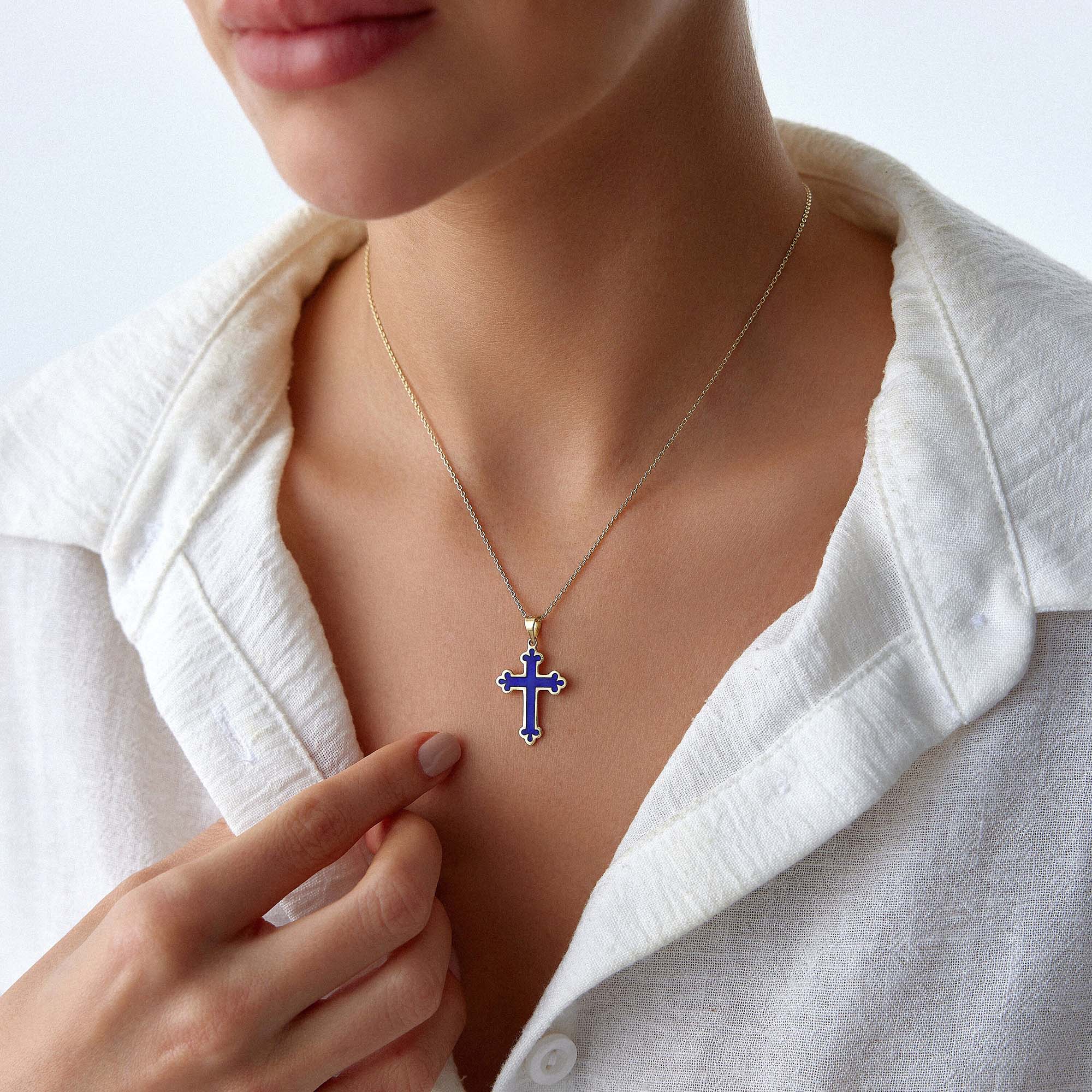 A model wearing a 14k yellow gold large navy blue cross pendant on a gold chain