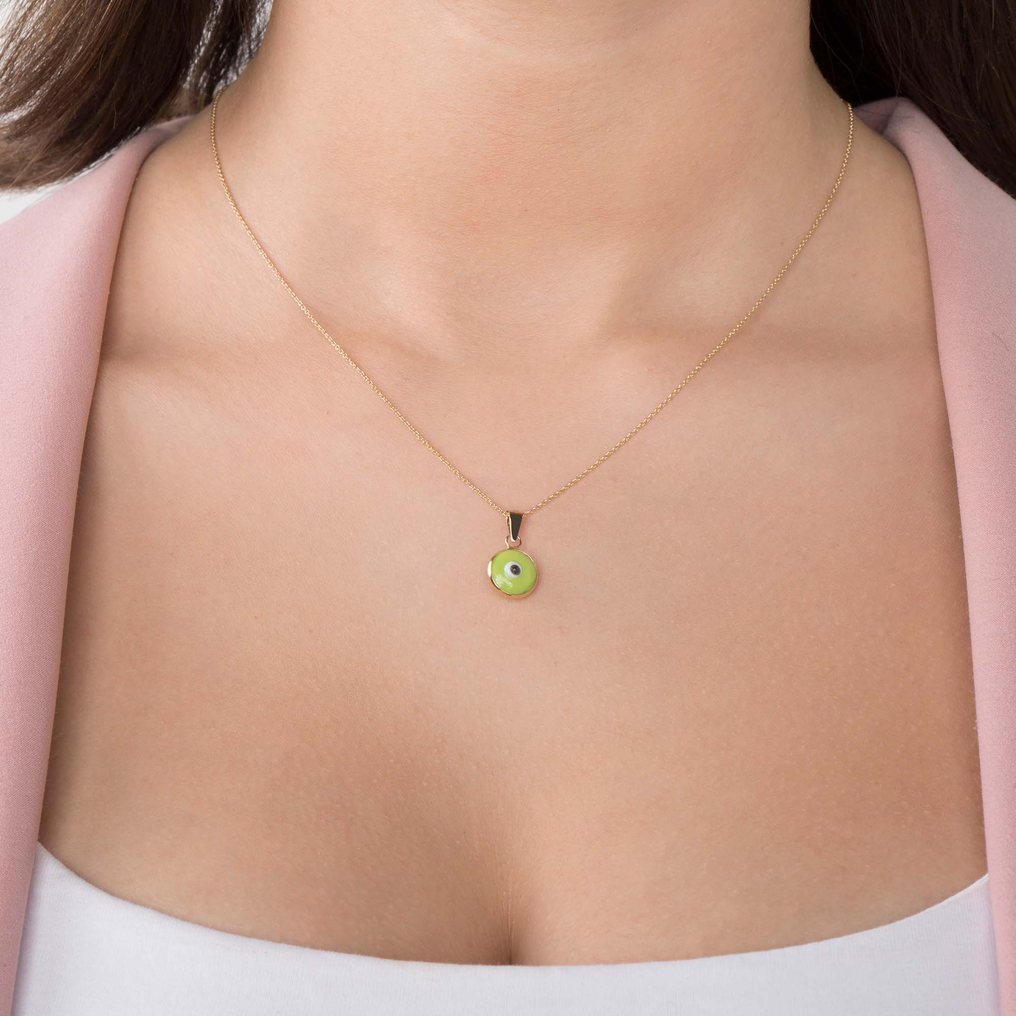 A model wearing a lime green evil eye pendant on a thin gold chain