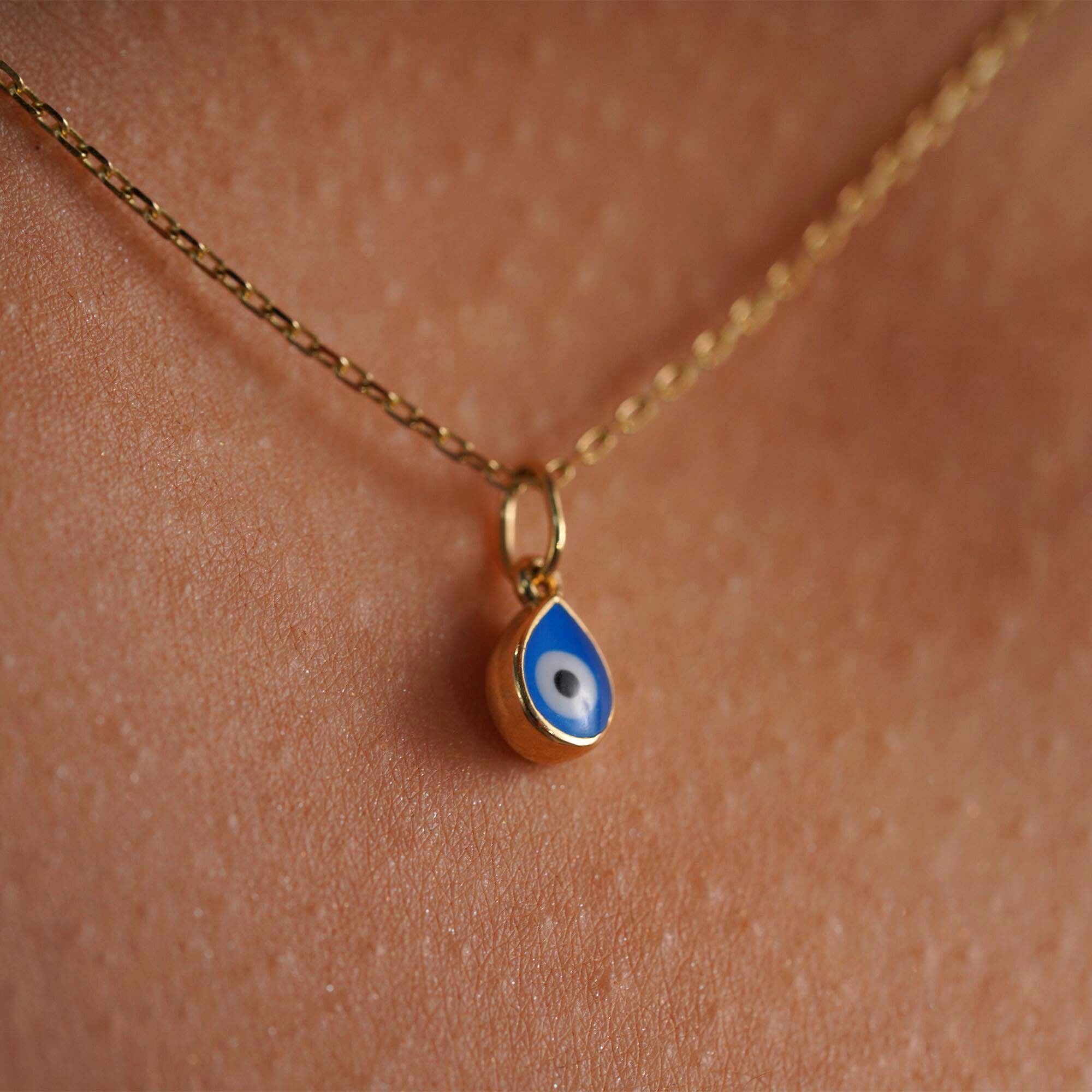 An up-close image of a raindrop evil eye pendant on a thin gold chain