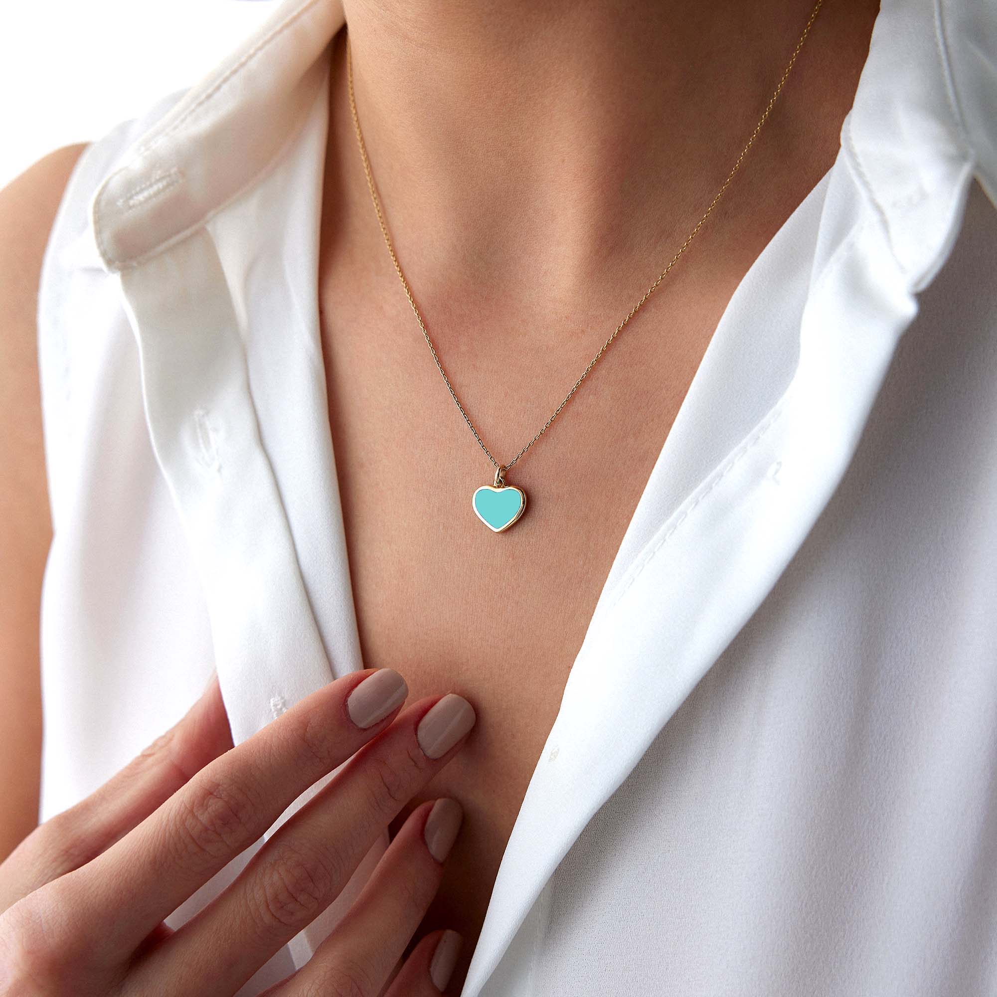 Necklace with a heart-shaped turquoise enamel pendant worn by a person in a white shirt.