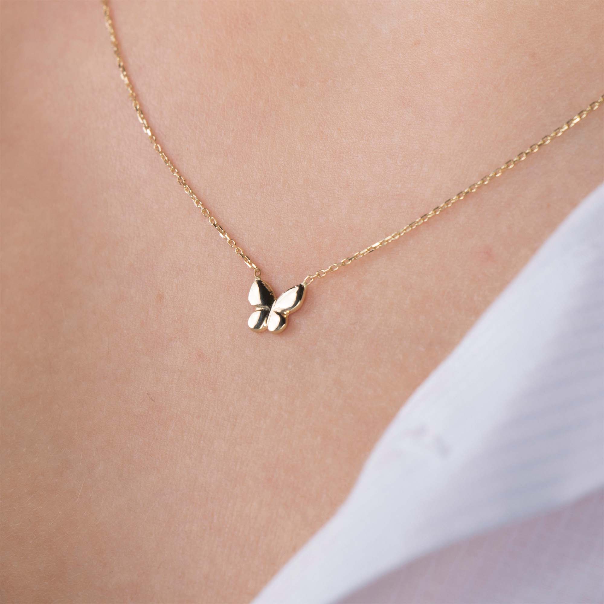 A minimal gold butterfly necklace on a person's neck with a white shirt background