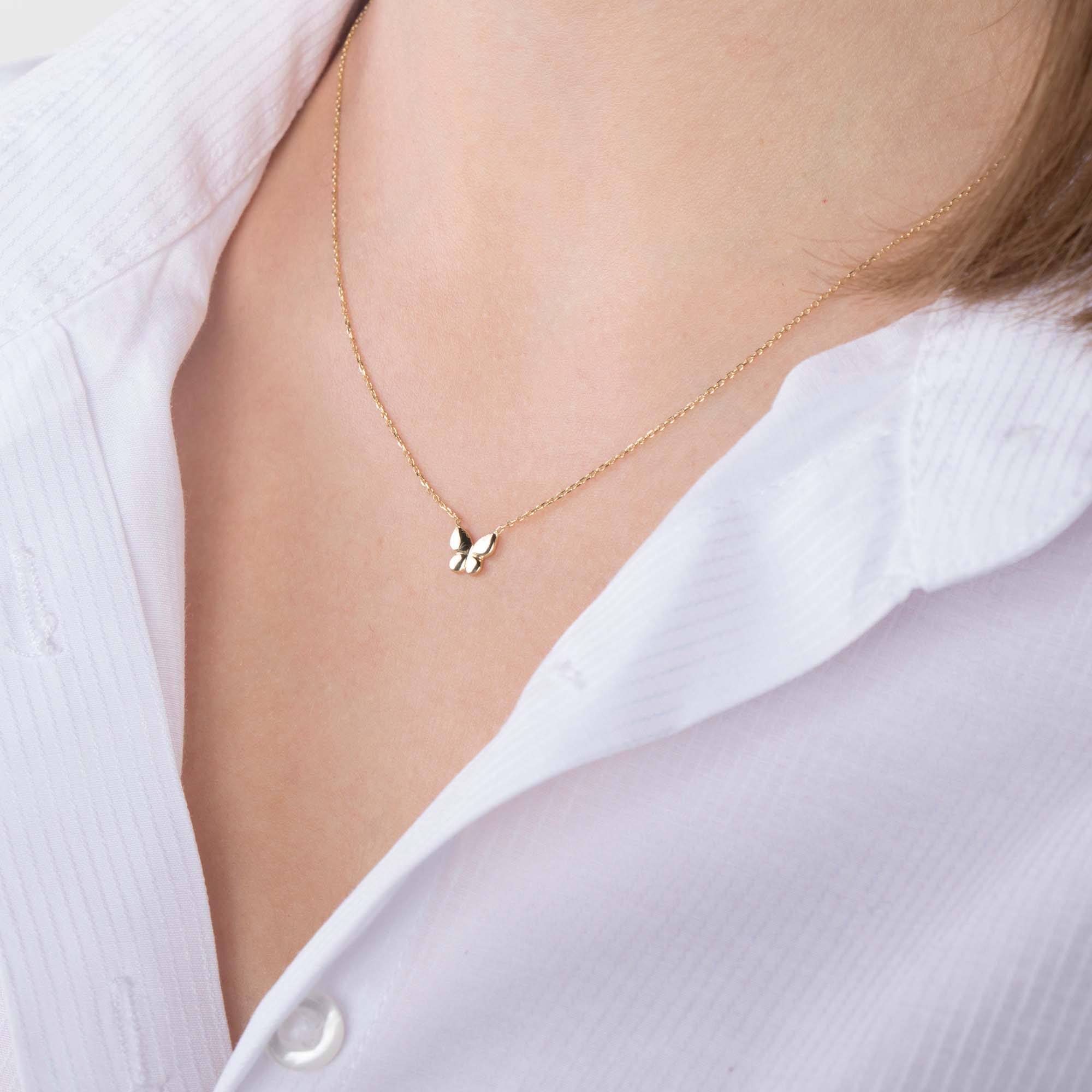 A minimal gold butterfly necklace on a person's neck with a white shirt background