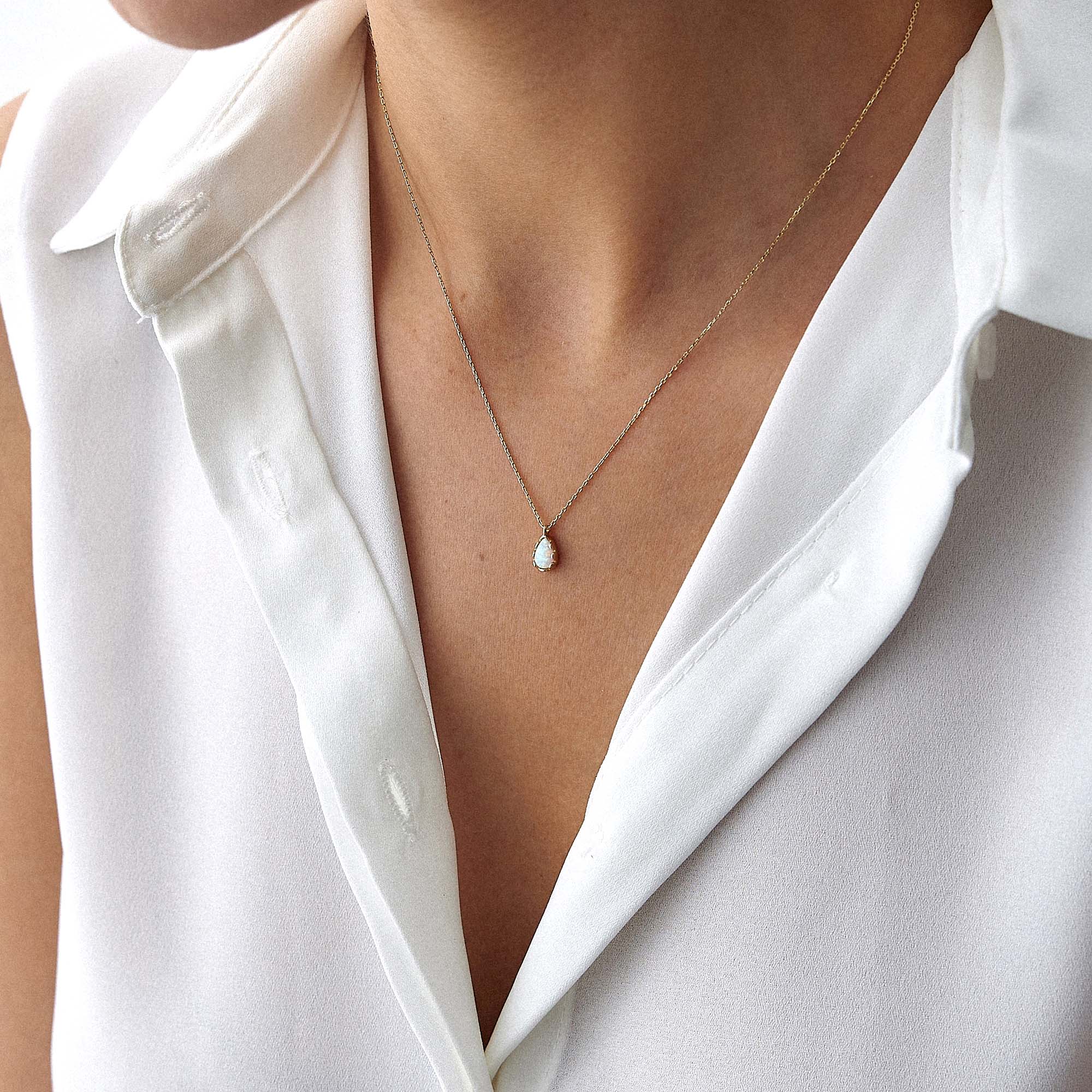 An up-close image of a model wearing a raindrop shaped opal necklace.