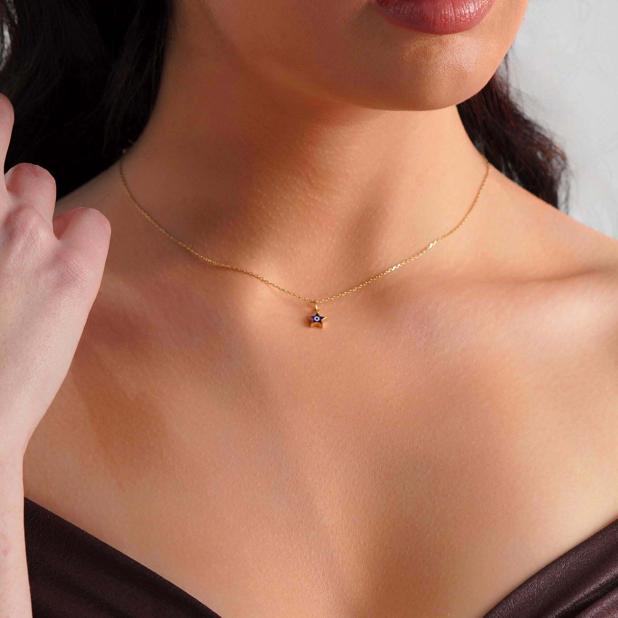 A model wearing a tiny star pendant with an evil eye center on a thin gold chain