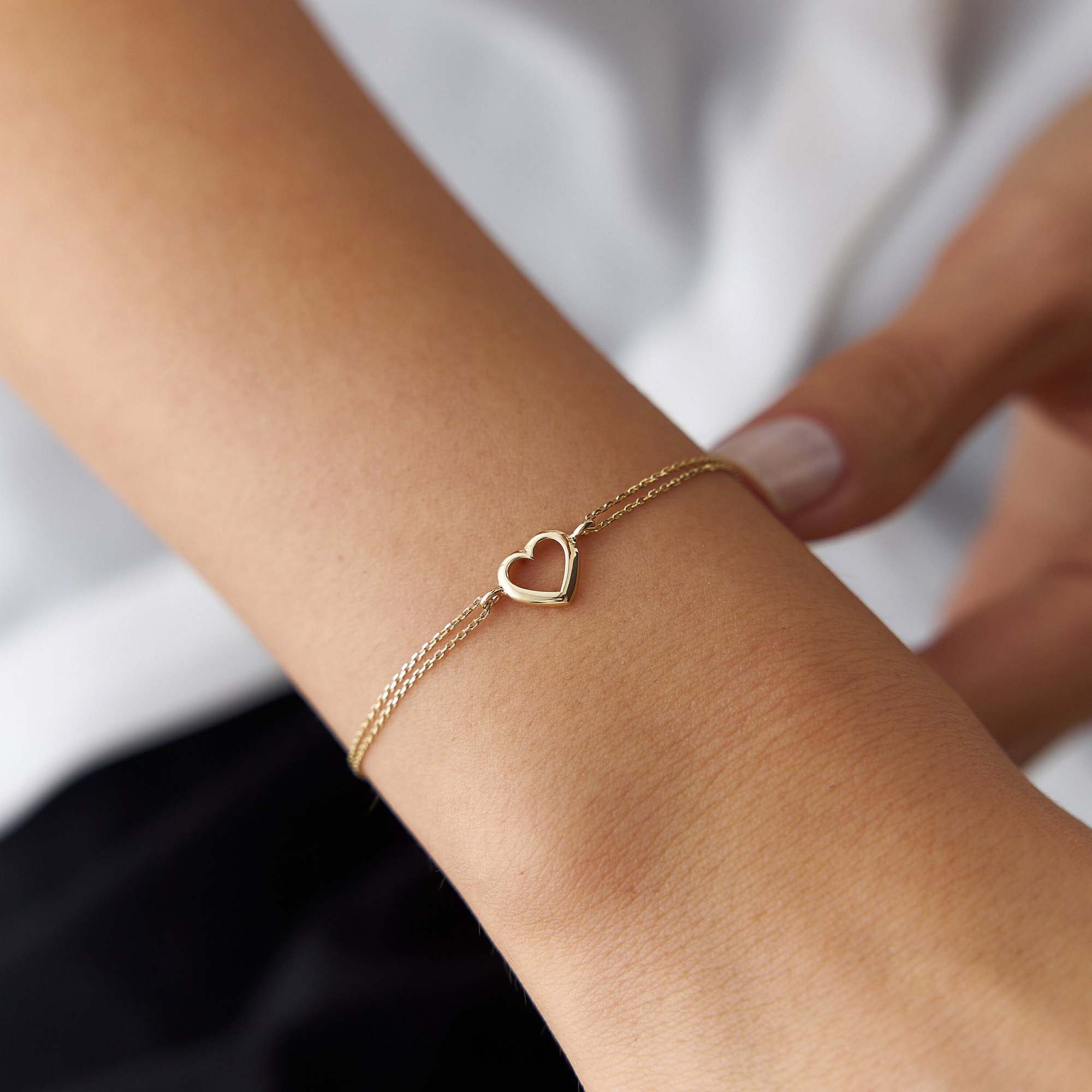 Gold bracelet with a heart charm on a wrist against a white background