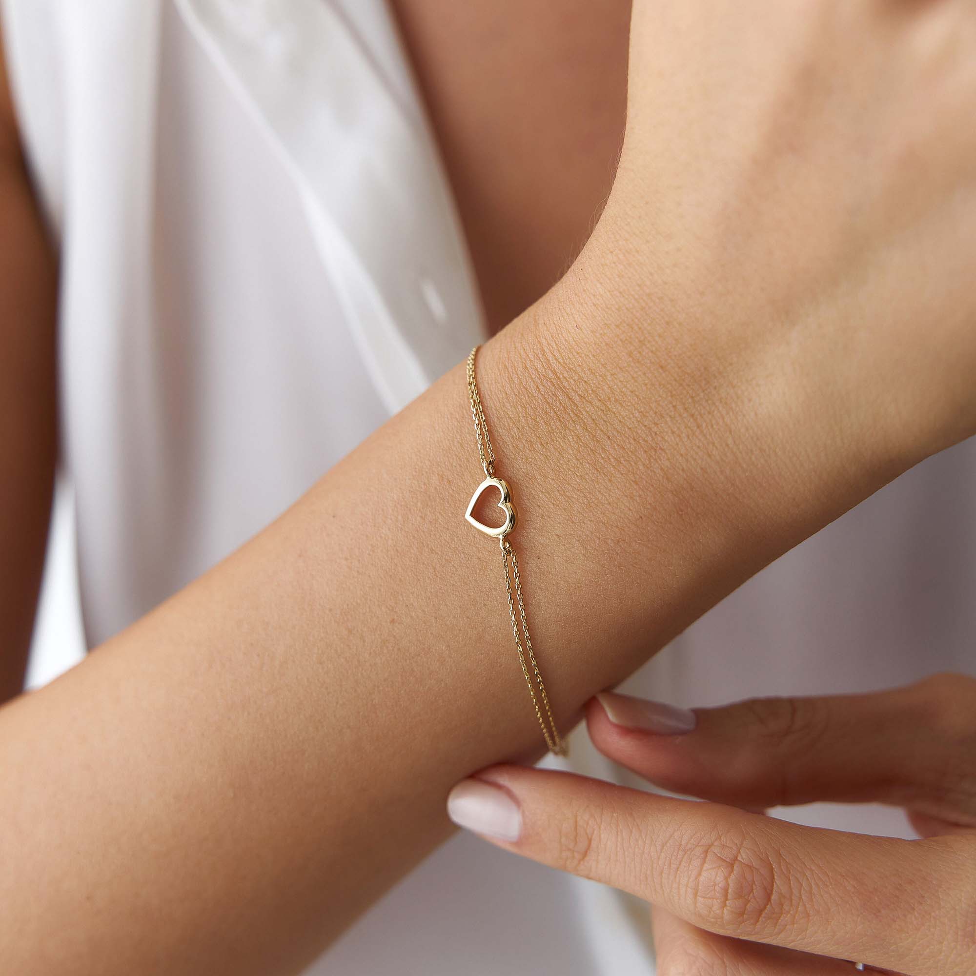 Gold bracelet with a heart charm on a wrist against a white background
