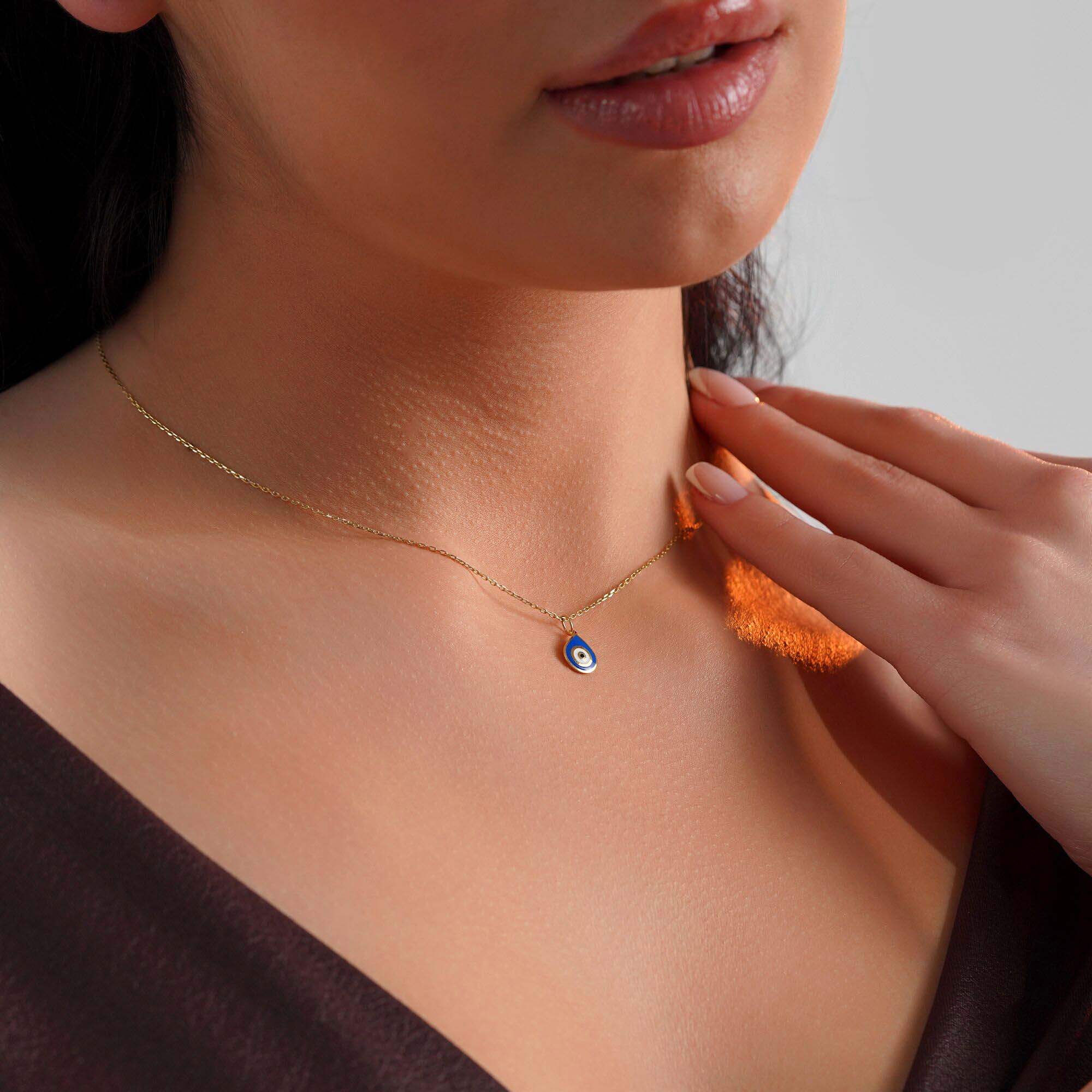 Close-up of a model wearing a raindrop pendant with an evil eye center on a thin gold chain.