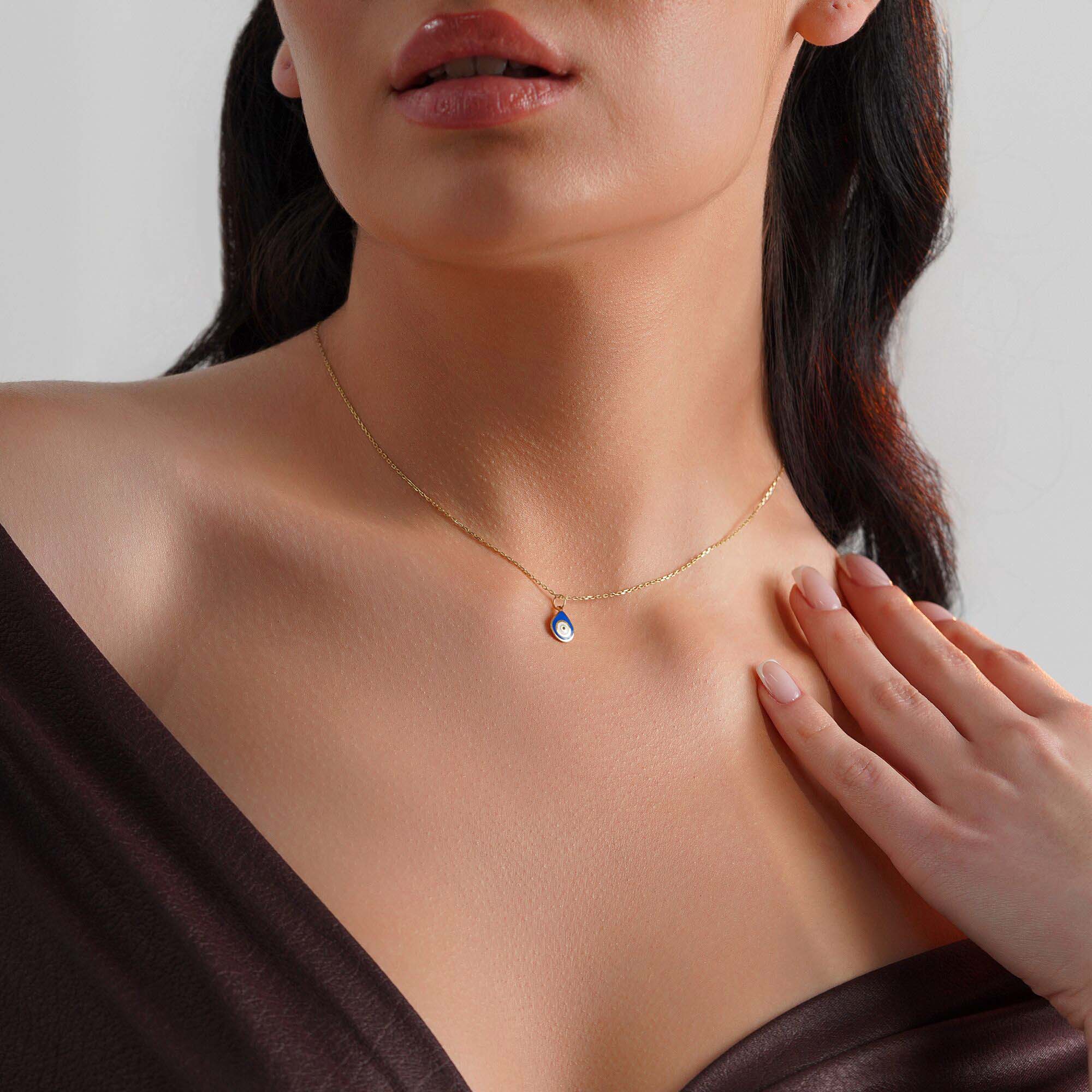 Close-up of a model wearing a raindrop pendant with an evil eye center on a thin gold chain.