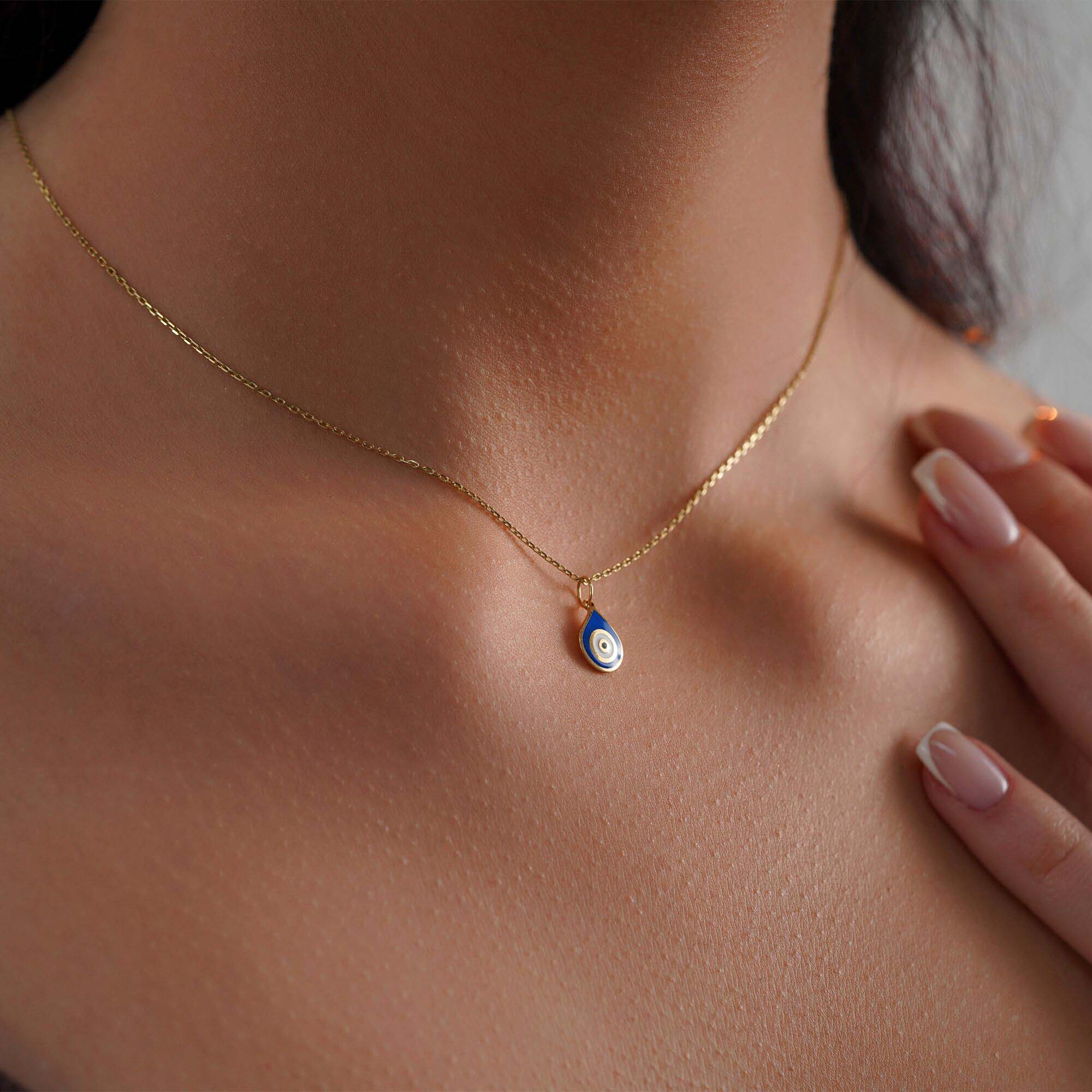 Close-up of a model wearing a raindrop pendant with an evil eye center on a thin gold chain.