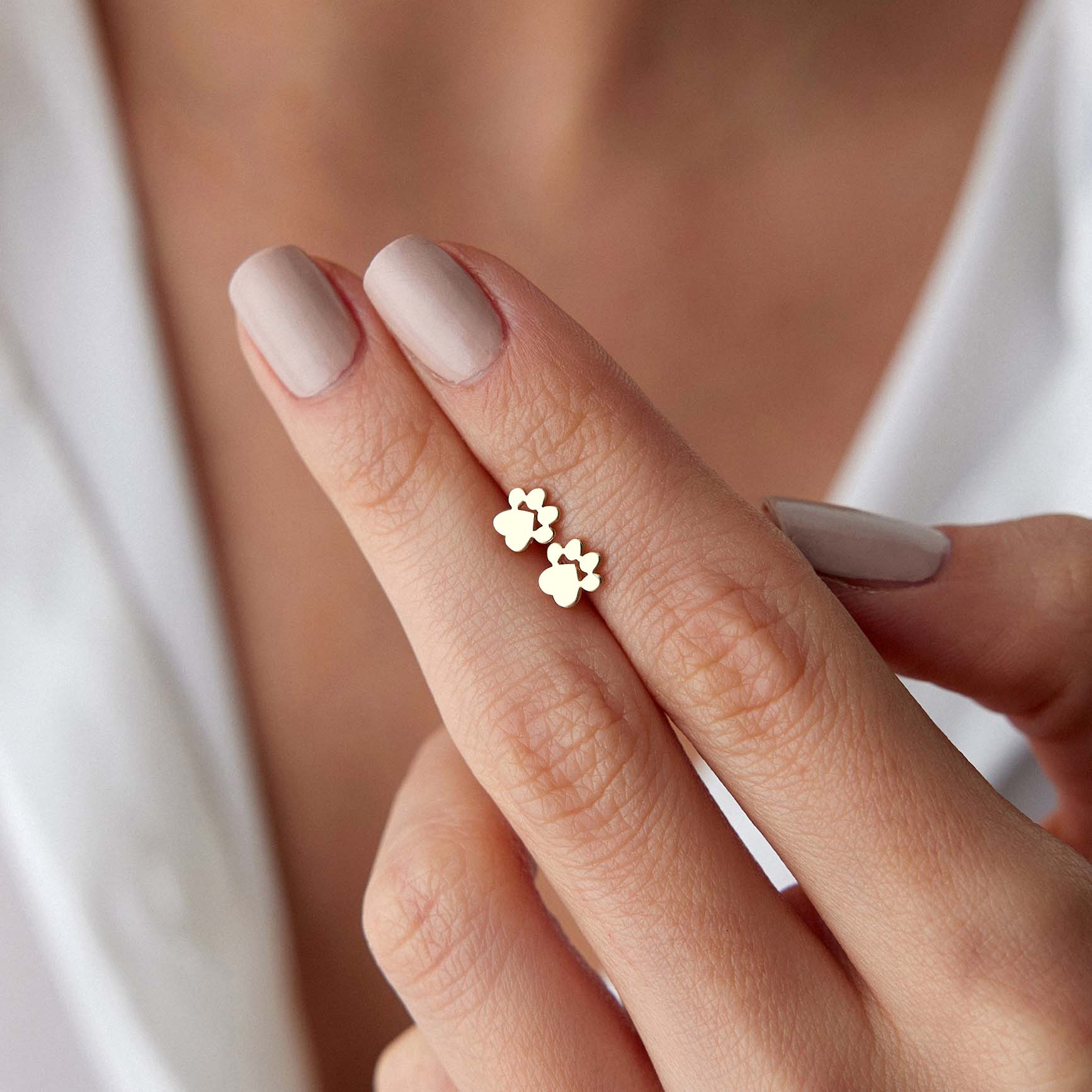 Gold paw print earrings on a finger with a blurred background