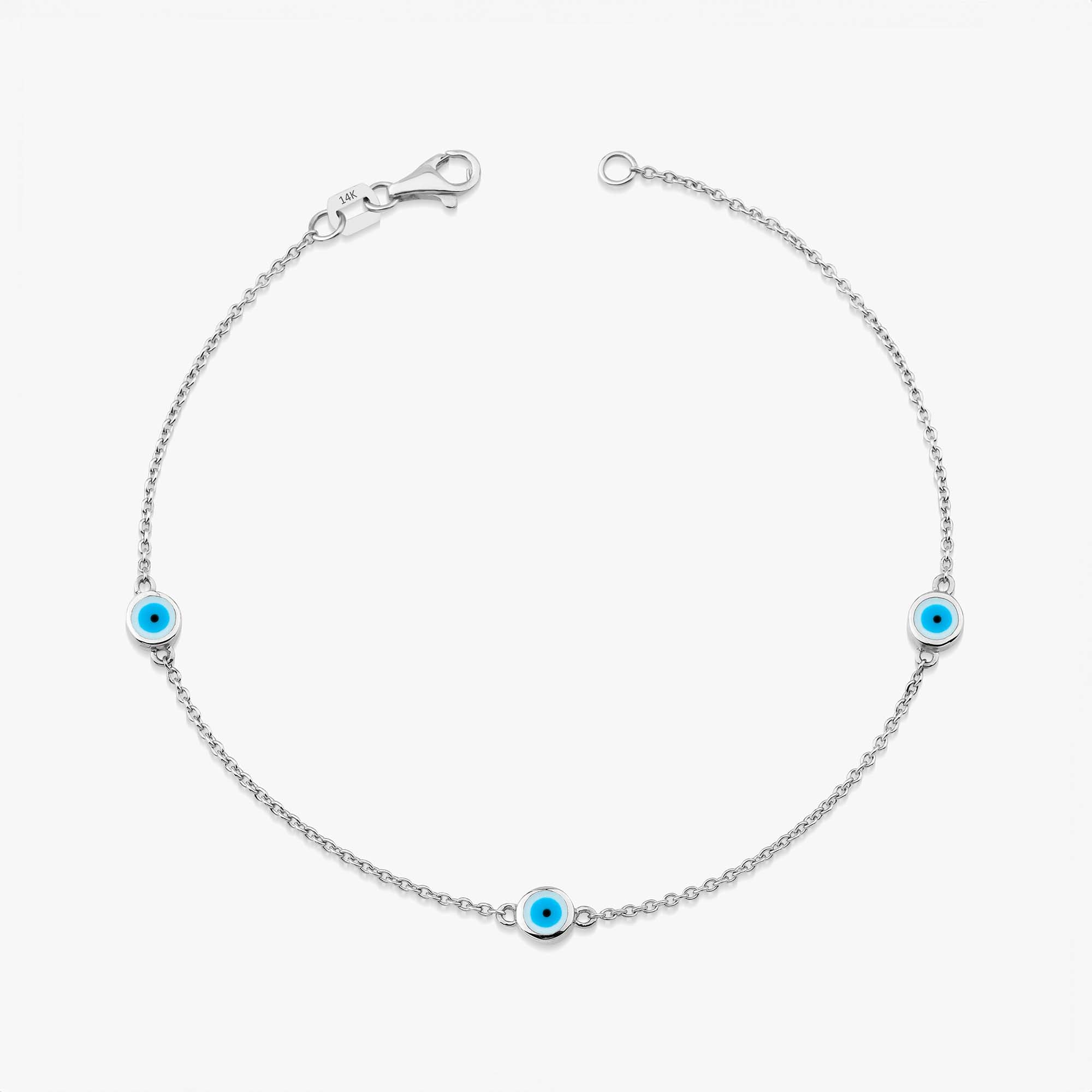 A 14 karat white gold bracelet with three white evil eye charms on a white background
