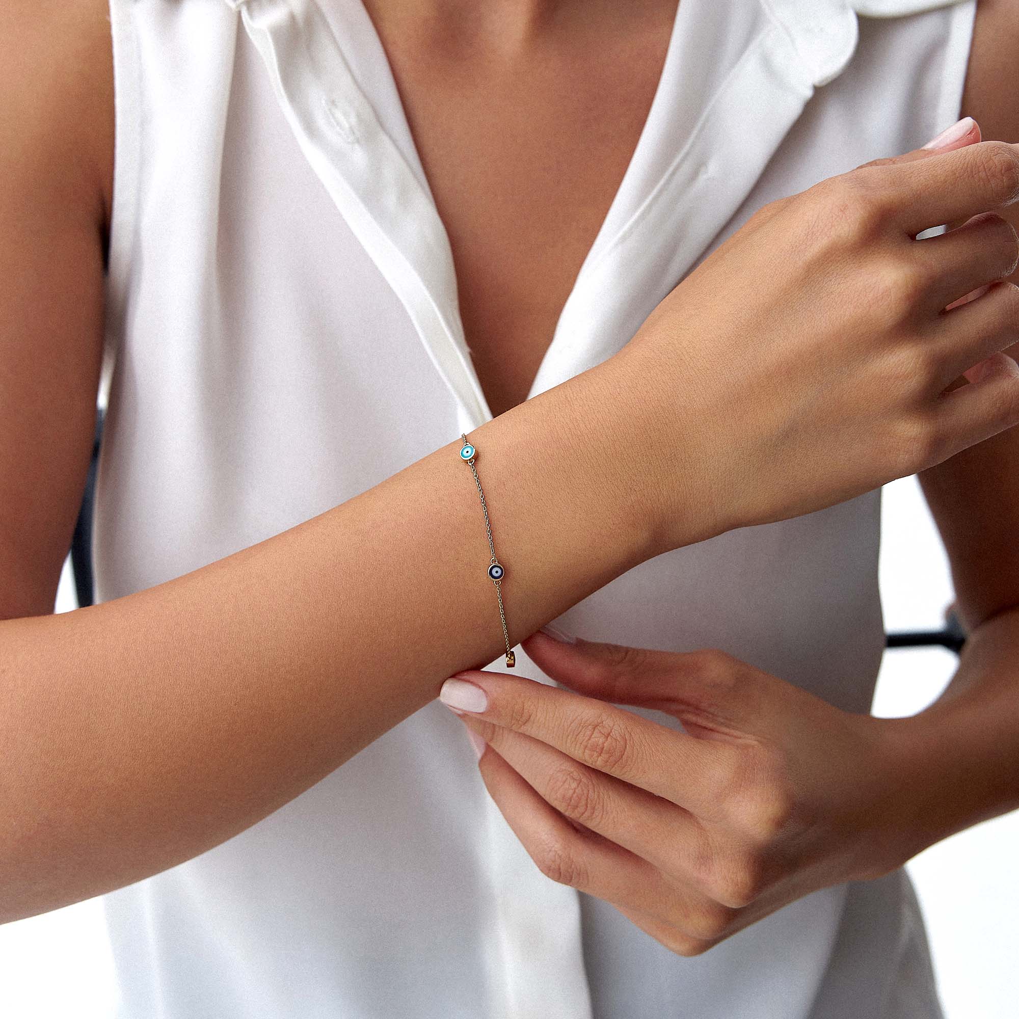 A 14K gold bracelet with five multicolored enamel evil eyes, featuring a chain design, on a wrist.