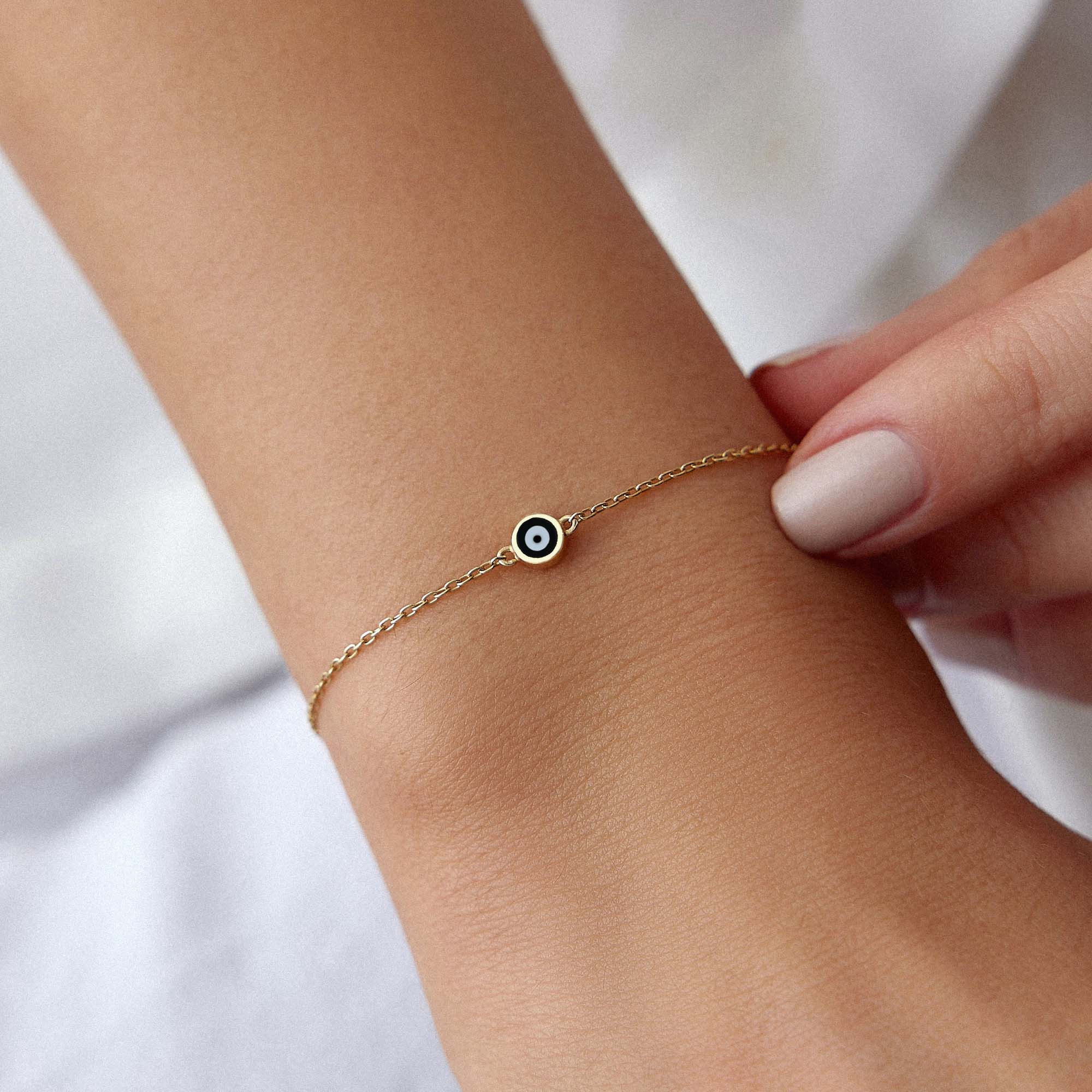 A 14K gold evil eye bracelet with a minimal black enamel evil eye design on a wrist