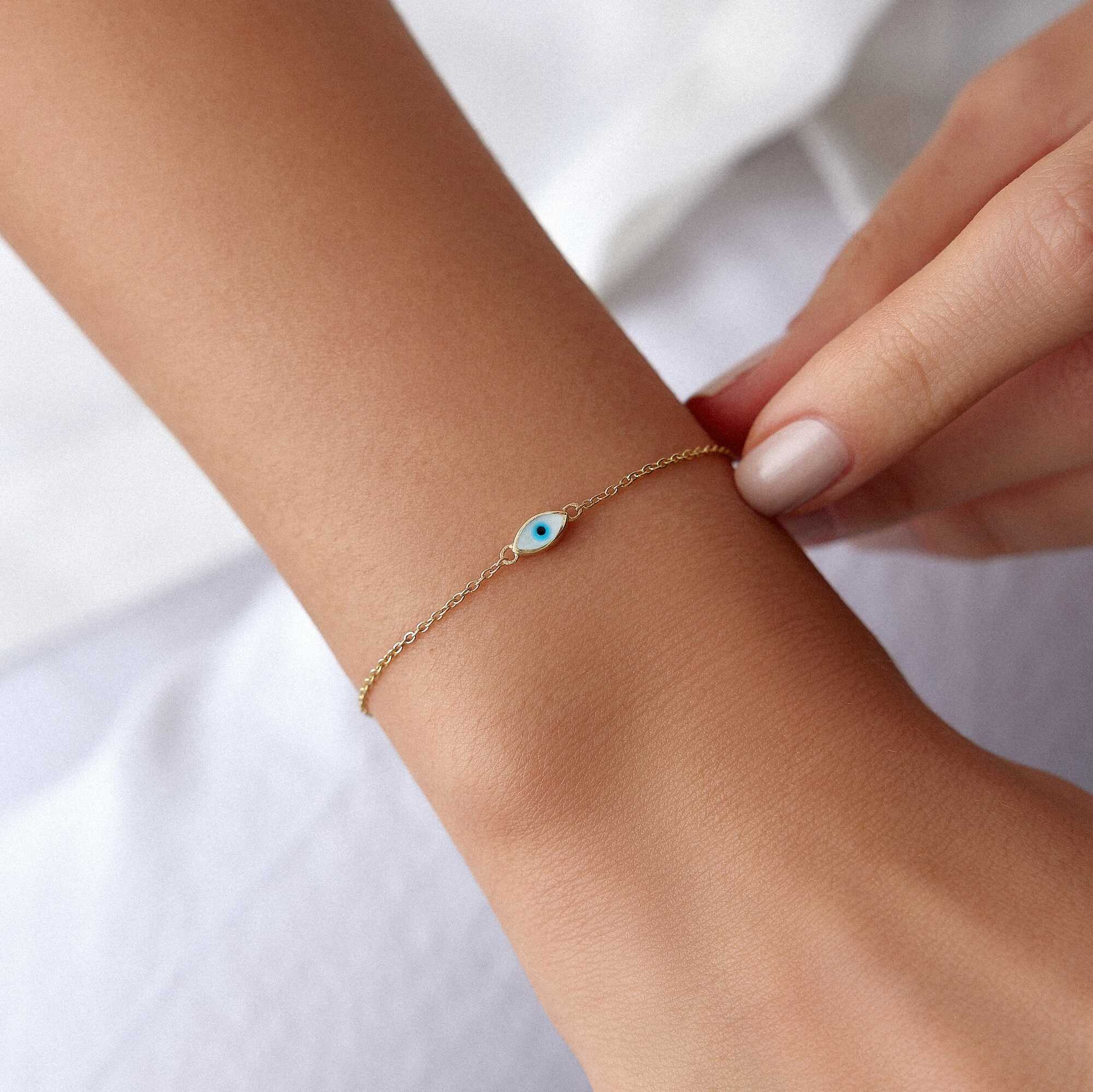 A 14K gold solid evil eye bracelet with white enamel accents, featuring a double-sided design with eyes on both sides, on a model's wrist.