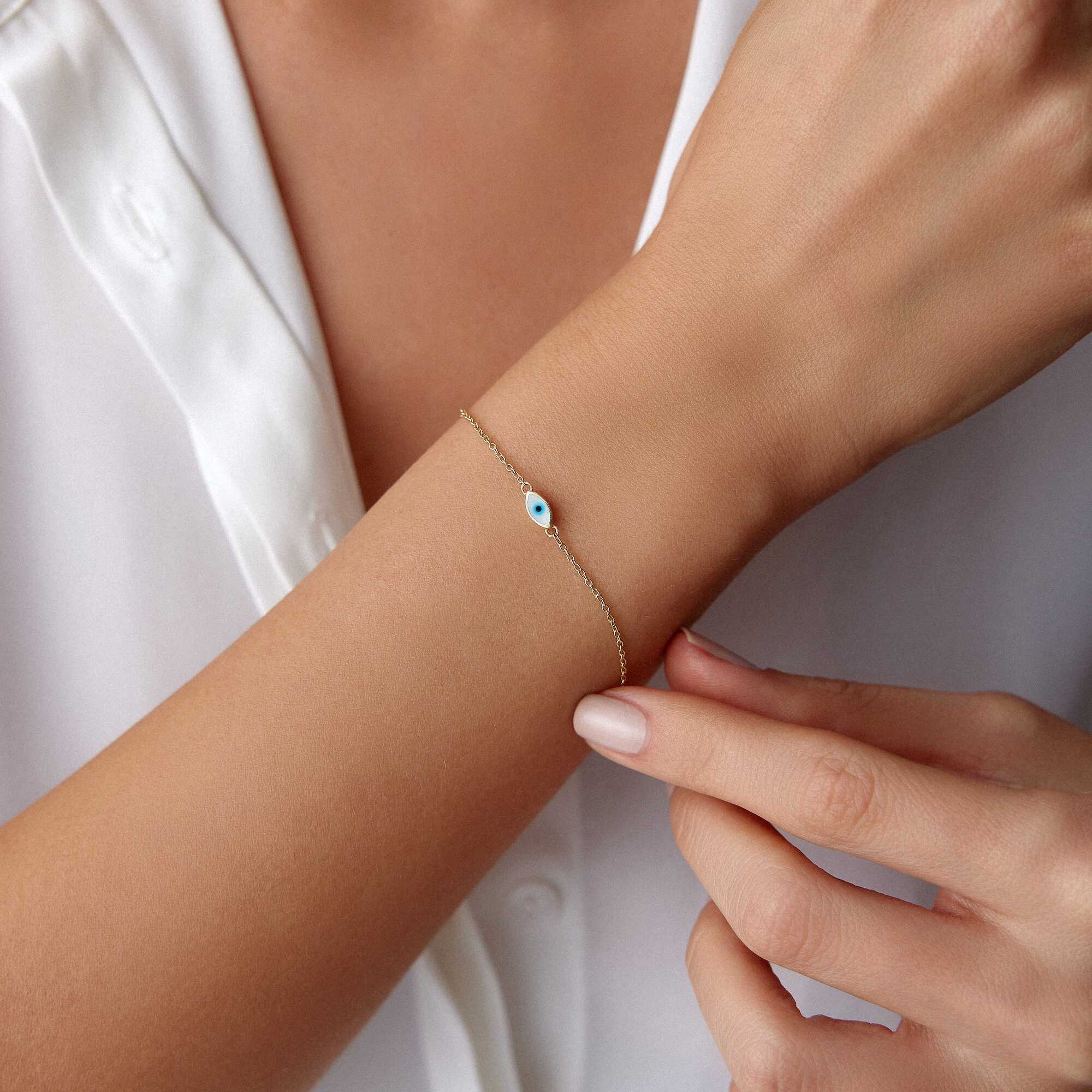 A 14K gold solid evil eye bracelet with white enamel accents, featuring a double-sided design with eyes on both sides, on a model's wrist.