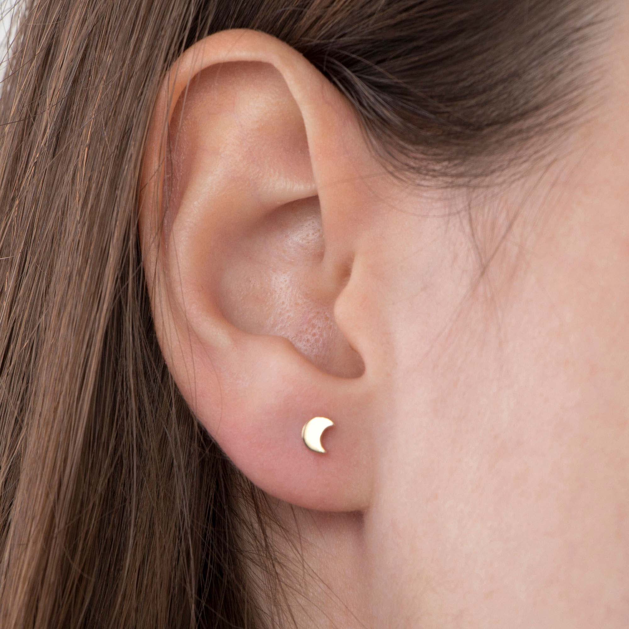 Gold crescent moon earring worn by a person with brown hair.