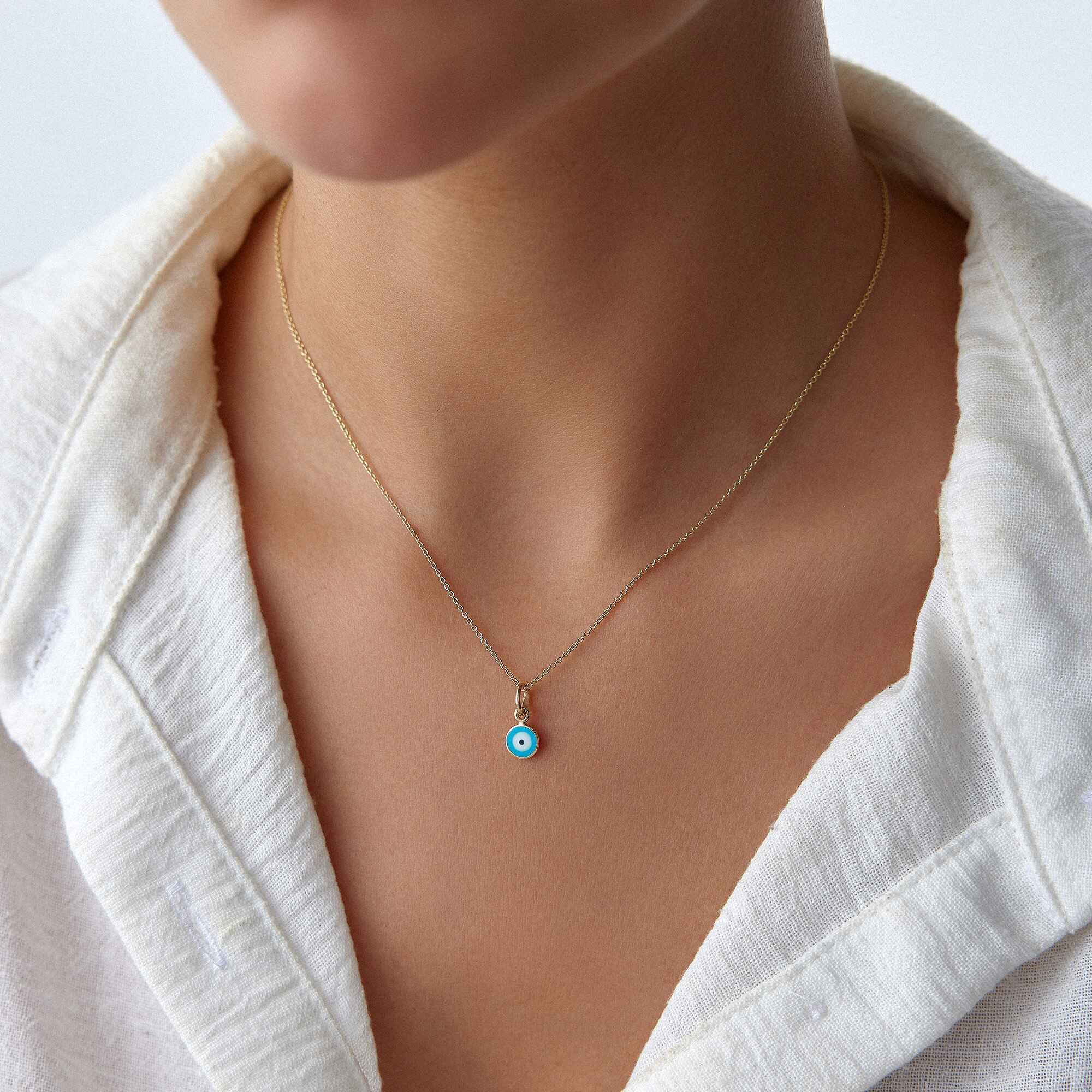 A model wearing a minimal ocean blue evil eye pendant on a thin gold chain.