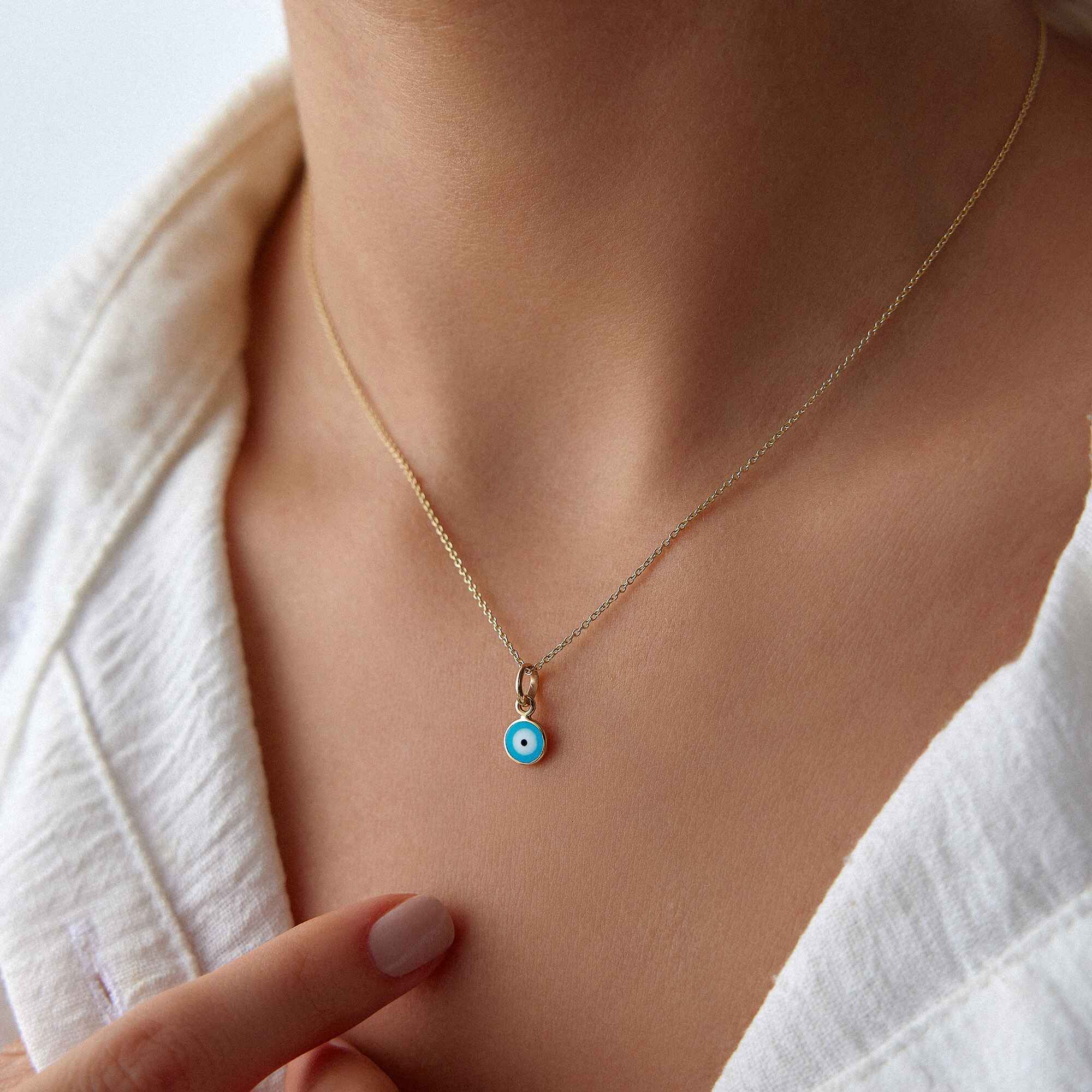 A model wearing a minimal ocean blue evil eye pendant on a thin gold chain.