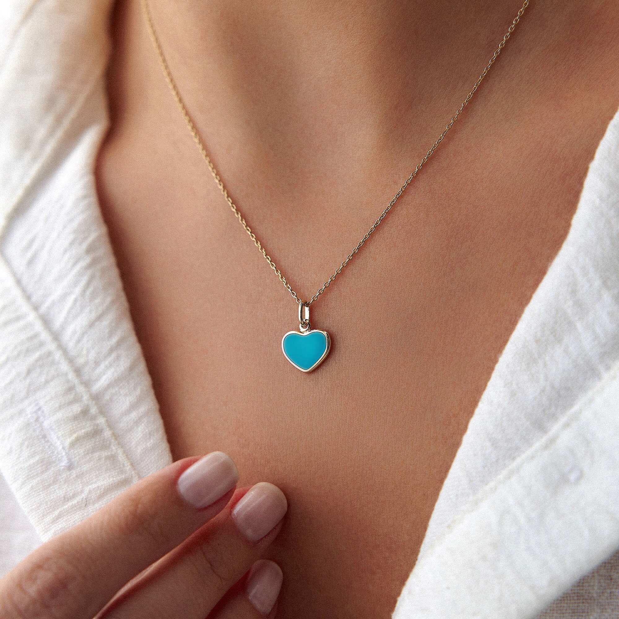 A 14k yellow gold ocean blue heart pendant worn by a model on a thin gold chain.