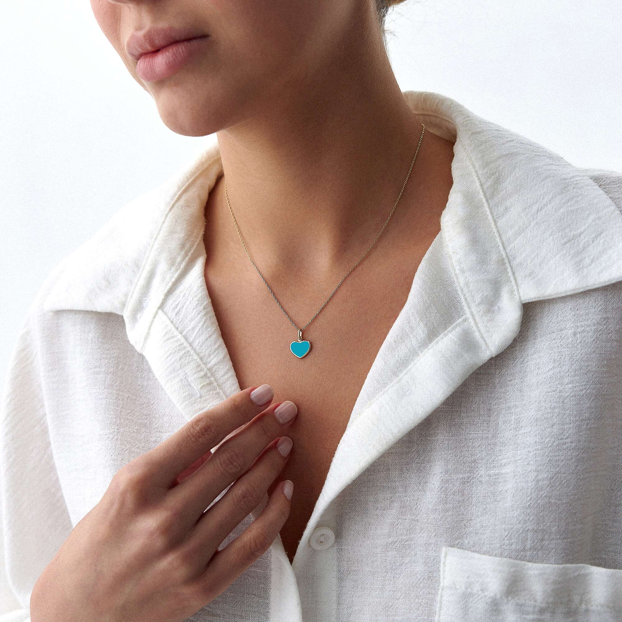 A 14k yellow gold ocean blue heart pendant worn by a model on a thin gold chain.