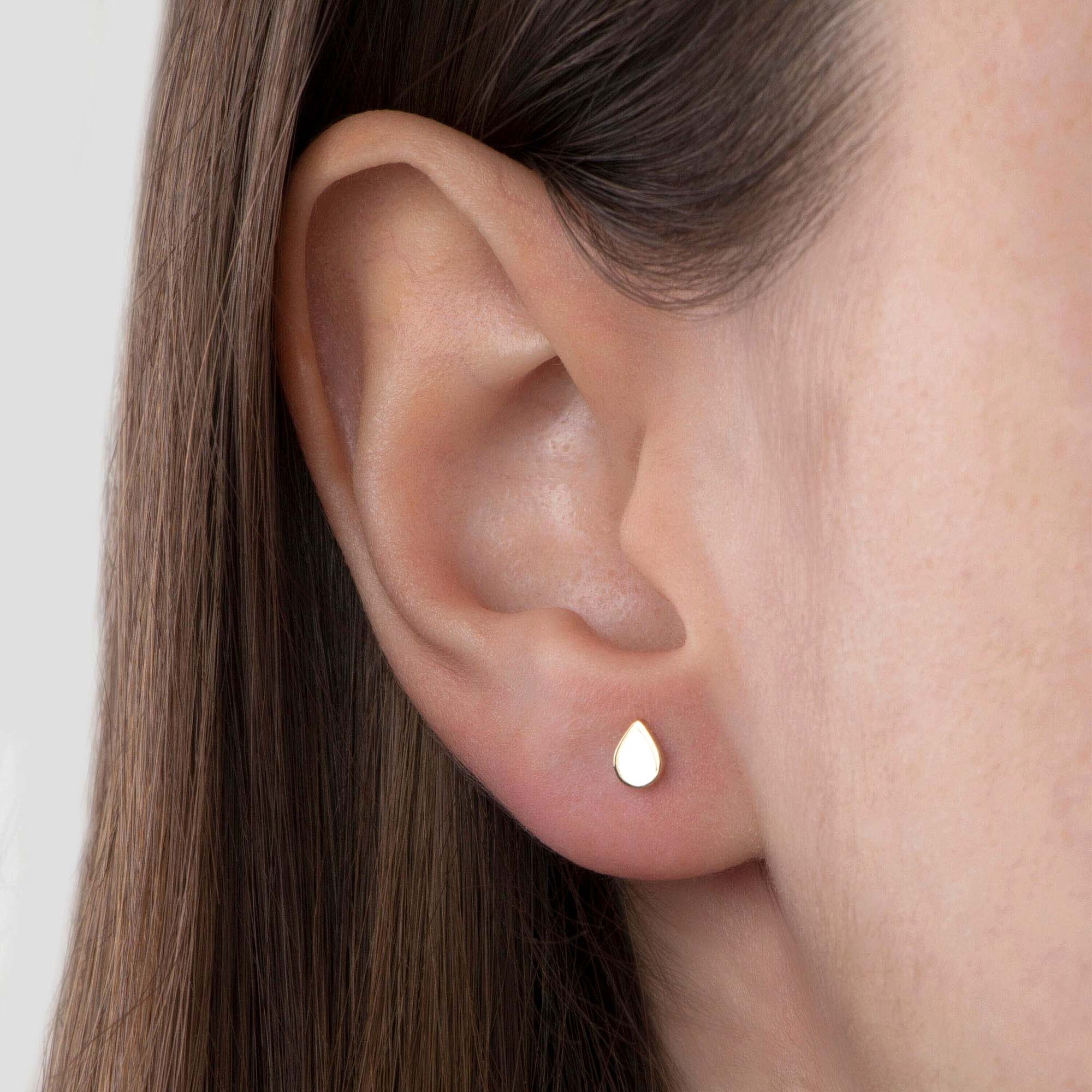 Close-up of an ear wearing a small raindrop-shaped earring.