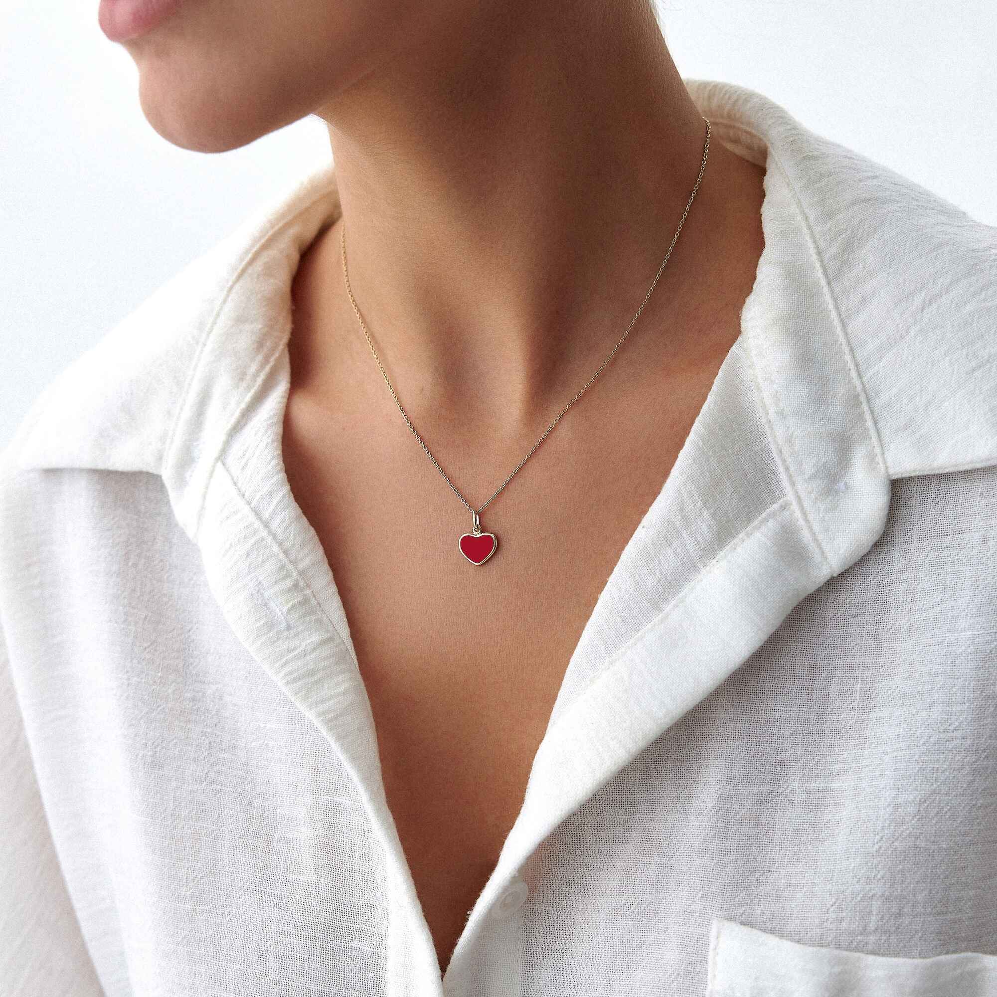 A model wearing a 14k yellow gold red enamel heart pendant worn on a thin gold chain