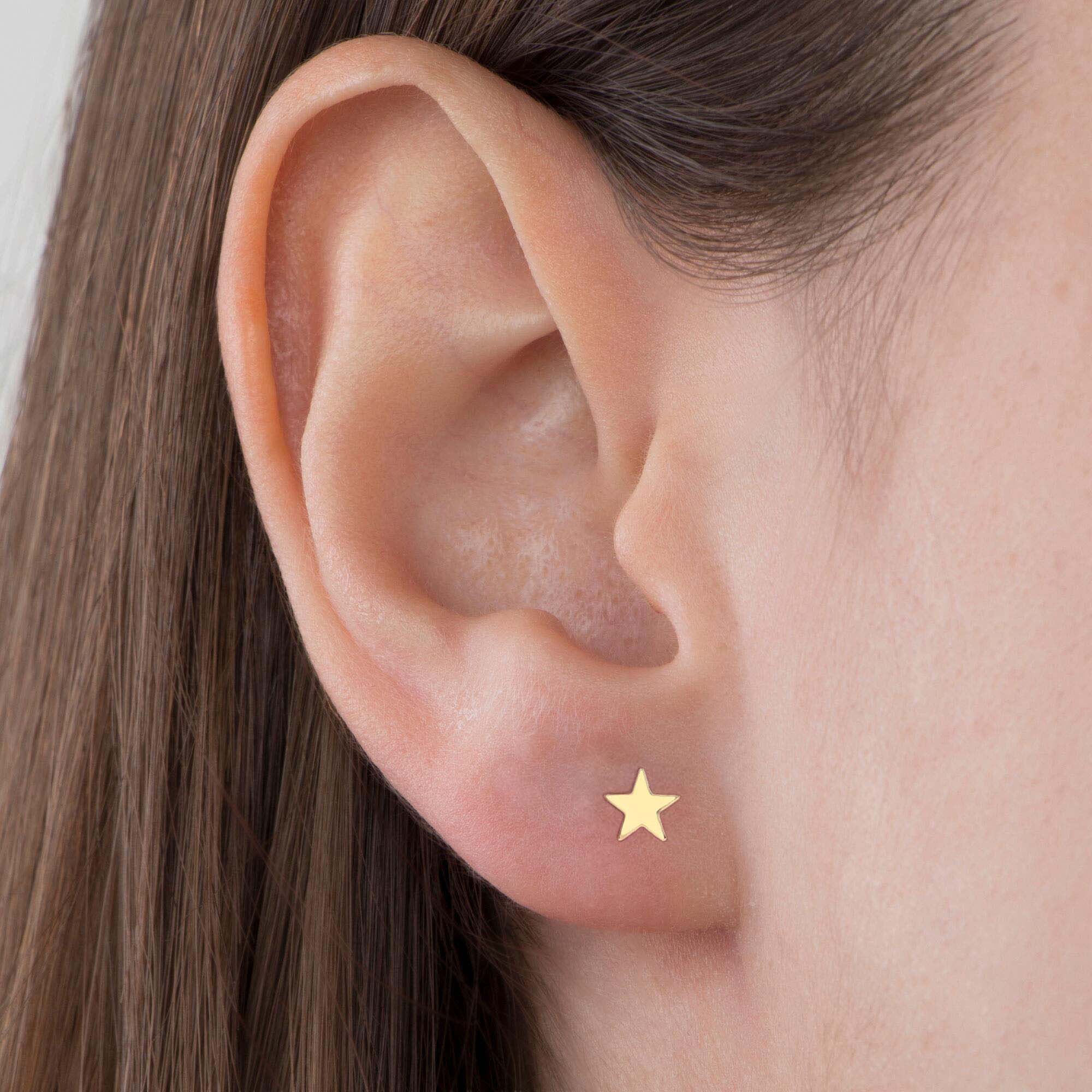 Close-up of an ear wearing a gold star-shaped earring with a neutral background